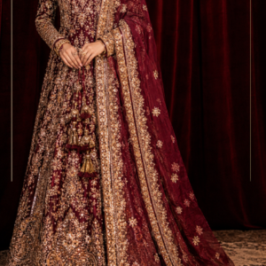 i suitsMeher-e-Maharani – Deep Maroon Luxury Anarkali Suit Step into timeless Indian elegance with Meher-e-Maharani, a magnificent deep maroon embroidered Anarkali suit created by Maharani Designer Boutique for women who appreciate rich colours, intricate craftsmanship, traditional silhouettes, and luxurious occasion wear. This regal ensemble features a deep maroon Anarkali-style outfit covered with elaborate gold-toned embroidery, a beautifully coordinated sheer dupatta, and ornate borders that create a sophisticated couture-inspired appearance. The richness of the maroon base provides the perfect canvas for the extensive golden embroidery, allowing every motif, border, and decorative detail to stand out beautifully. The outfit showcases an elegant full-length silhouette with a graceful flare, a richly embellished neckline, long embroidered sleeves, an intricately decorated lower section, and a statement dupatta. The combination creates a complete traditional Indian look that feels luxurious, feminine, and timeless. The design is especially suited to weddings, wedding receptions, engagement celebrations, sangeet functions, festive gatherings, formal dinners, family celebrations, and other special occasions. From the elaborate neckline to the detailed sleeves, ornate skirt panels, decorative hem, and richly bordered dupatta, every visible element contributes to the grandeur of this ensemble. Meher-e-Maharani is designed for the woman who wants her Indian occasion wear to make a statement through craftsmanship, colour, and elegance. The Richness of Deep Maroon The deep maroon colour is the defining foundation of this ensemble. Maroon has long been associated with luxury, sophistication, celebration, and traditional Indian fashion. Its deep jewel-like character creates a dramatic appearance while remaining more refined and understated than brighter shades of red. In this design, the maroon base provides a striking contrast against the gold-toned embroidery. The combination of deep maroon and gold immediately creates a regal aesthetic. It is particularly suitable for women who prefer rich, mature colours and want an outfit that feels luxurious without relying on excessive colour variation. The colour is especially beautiful for evening celebrations, where warm lighting can enhance the depth of the maroon fabric and allow the gold embellishment to create a subtle luminous effect. For wedding receptions, formal dinners, and grand celebrations, this colour combination offers an elegant alternative to conventional bridal red. Intricate Gold Embroidery The most prominent characteristic of this designer Anarkali is its elaborate gold-toned embroidery. The embroidery is distributed throughout the garment, creating a richly detailed surface while maintaining a carefully balanced composition. Floral-inspired motifs, ornamental patterns, scrolling details, paisley-like elements, and traditional decorative forms appear across the outfit. The upper portion features intricate embroidery around the neckline and bodice, creating an elegant frame around the face and jewellery. The sleeves continue the same embroidery language, with detailed motifs extending towards the cuffs. Across the flowing lower portion, the embroidery becomes progressively richer, creating a beautiful sense of movement and visual depth. The lower borders feature especially elaborate decorative work, giving the outfit a grand and finished appearance. This extensive detailing makes the ensemble particularly suitable for women looking for heavy embroidered Anarkali suits and luxury Indian occasion wear. MDB 024717,Emerald Green & Deep Red Bridal Lehenga,MDB 024311 ,MDB 027210162,MDB 027210130 Elegant Anarkali Silhouette The Anarkali silhouette is one of the most timeless forms in Indian fashion. This ensemble uses a graceful full-length silhouette that begins with a fitted or structured upper section and gradually opens into a flowing flare. The silhouette creates an elongated appearance while providing generous movement through the lower portion. The flare is particularly beautiful when the wearer walks because the embroidered panels move naturally and allow different sections of the design to become visible. This creates a dramatic effect without compromising the elegance of the overall outfit. The Anarkali silhouette also provides a beautiful foundation for traditional Indian embroidery because the large surface area allows motifs and borders to be arranged in a balanced way. The result is a garment that feels traditional, graceful, and luxurious while remaining suitable for contemporary styling. Ornate Embroidered Neckline The neckline is one of the key focal points of the design. It features detailed gold embroidery arranged around the neckline and extending into the front bodice. The intricate pattern creates a beautiful frame for traditional jewellery. A statement choker can sit elegantly above the neckline, while a longer necklace can be layered below it for a more elaborate bridal-inspired look. The embroidery around the neckline also means that the outfit remains visually striking even when styled with minimal jewellery. For a modern reception appearance, statement earrings can be worn without a necklace, allowing the neckline embroidery to remain the centre of attention. Heavily Embellished Sleeves The long sleeves add a sophisticated and regal character to the outfit. Rather than keeping the sleeves plain, the design carries detailed embroidery throughout the arms, creating continuity with the bodice and lower portion. The cuffs are particularly ornate and provide a beautifully finished appearance around the wrists. This styling works especially well with traditional bangles and bracelets. The full-sleeved silhouette also makes the ensemble an elegant choice for formal evening occasions and winter celebrations. The detailed sleeves add visual richness without changing the graceful proportions of the Anarkali. Detailed Lower Panels The lower portion of the Anarkali is richly decorated with elaborate embroidery. Large traditional-inspired motifs are arranged across the flowing panels, creating visual focal points as the skirt expands towards the floor. Between the larger motifs, smaller floral and ornamental patterns fill the space, creating a cohesive embroidered surface. The placement of the embroidery creates a beautiful sense of rhythm. Some areas feature denser detailing, while other sections allow the maroon base to remain visible. This balance prevents the outfit from appearing visually overwhelming despite the extensive embroidery. The lower section is especially striking in full-length photographs because the flowing panels create movement while the embroidery adds texture and depth. Statement Embroidered Hem The hemline is one of the most richly detailed areas of the outfit. A broad decorative border runs around the bottom of the Anarkali, creating a strong visual foundation. The border features multiple layers of intricate gold-toned embroidery, including floral and ornamental patterns. This multi-layered finish gives the outfit a couture-inspired appearance. When the Anarkali moves, the decorated hem becomes a beautiful focal point, especially in photographs and during a wedding entrance. The border also visually anchors the flowing silhouette and provides a clear finishing line around the garment. Richly Embellished Dupatta The coordinated dupatta completes the outfit and adds another layer of elegance. The deep maroon dupatta is designed with an ornate gold border that runs along its length. The border contains intricate embroidery and decorative motifs that complement the main Anarkali. Additional motifs are scattered across the dupatta, creating subtle detailing throughout the fabric. The sheer appearance of the dupatta allows it to fall gracefully while keeping the overall look light enough to maintain movement. The dupatta can be styled traditionally over the head for a ceremonial appearance or draped over one shoulder for a sophisticated contemporary look. For a wedding reception, the border can be arranged prominently across the front to showcase the embroidery. Traditional Indian Craftsmanship The overall design reflects the beauty of traditional Indian occasion wear, where colour, embroidery, silhouette, and finishing work together to create a complete look. The deep maroon base represents the richness of traditional Indian clothing. The gold embroidery introduces luxury. The Anarkali silhouette creates grace and movement. The ornate dupatta adds dimension. The elaborate borders provide structure and finishing. Together, these elements create an ensemble that feels rooted in Indian heritage while remaining suitable for modern celebrations. Perfect for Weddings This deep maroon designer Anarkali suit is a versatile option for wedding celebrations. It can be worn for: Wedding receptions Engagement ceremonies Sangeet functions Mehendi celebrations Family weddings Pre-wedding events Formal dinners Festive celebrations Destination weddings Anniversary celebrations Cultural events Wedding guest occasions The richness of the embroidery makes it suitable for formal events, while the classic silhouette allows it to be styled according to the specific function. For a daytime celebration, pair it with lighter jewellery and soft makeup. For an evening reception, add statement jewellery and a more glamorous beauty look. Ideal for Wedding Receptions Wedding receptions are perfect occasions for deep maroon and gold. The colour combination creates an elegant evening appearance, while the embroidery catches the light beautifully. For a reception, style the Anarkali with a statement choker, large earrings, a sleek clutch, and metallic footwear. A polished low bun can create a sophisticated appearance, while soft waves can make the look more romantic. The dupatta can be draped over one shoulder to reveal the detailed neckline and sleeves. Elegant Engagement Wear For engagement ceremonies, this ensemble can be styled in a more refined way. The deep maroon colour provides sophistication, while the intricate embroidery adds the required festive character. Pair it with a statement necklace and matching earrings for a traditional appearance. Alternatively, wear oversized earrings and skip the necklace for a modern look. A maang tikka can be added for a more traditional Indian styling. Soft waves or a sleek low bun can complete the look. Sangeet Styling The flowing Anarkali silhouette creates beautiful movement, making it suitable for sangeet celebrations. For a glamorous sangeet look, wear the dupatta over one shoulder and pair the outfit with statement earrings. The flowing lower portion allows the outfit to move gracefully while walking and dancing. A sleek hairstyle and luminous makeup can give the outfit a contemporary party appearance. For a more traditional look, add bangles, a choker, and a maang tikka. Festive Occasion Wear The versatility of the deep maroon colour makes this ensemble suitable beyond weddings. It can be styled for Diwali celebrations, family gatherings, festive dinners, cultural events, anniversary celebrations, and formal parties. For Diwali, pair it with gold jewellery and a metallic clutch. For a family celebration, choose more delicate jewellery and natural makeup. For a formal dinner, keep the accessories minimal and let the embroidery become the main statement. Jewellery Styling The extensive gold embroidery creates a natural connection with traditional gold jewellery. For a regal appearance, consider: Gold choker Kundan-inspired necklace Polki-style earrings Traditional jhumkas Maang tikka Bangles Statement rings Traditional nath The deep maroon colour can also complement jewellery featuring ruby-inspired, burgundy, or deep red accents. For a contemporary look, oversized gold earrings can be worn alone. The choice of jewellery can completely change the personality of the outfit. Hairstyle Suggestions A traditional centre-parted bun is an excellent choice for this Anarkali. The bun can be decorated with fresh flowers or traditional hair accessories. This hairstyle allows the neckline, earrings, and dupatta to remain clearly visible. For a reception, a polished low bun creates a sophisticated appearance. For an engagement or sangeet, soft waves provide a more contemporary and romantic finish. If the dupatta is worn over the head, a neat bun creates a clean and elegant foundation. Makeup Styling The deep maroon and gold palette works beautifully with warm and luminous makeup. Gold, bronze, champagne, and warm brown eyeshadows can complement the embroidery. Defined eyeliner and softly sculpted brows can enhance the eyes. A luminous complexion works particularly well with the reflective appearance of gold embroidery. For the lips, choose a deep rose, berry, wine, red, or nude shade depending on the desired look. For a traditional wedding appearance, a deeper lip can complement the richness of the outfit. For a modern reception, a softer rose or nude lip can create more balance. Photography-Friendly Design This ensemble is designed with numerous elements that create visual interest in photographs. The intricate neckline provides beautiful close-up detailing. The embroidered sleeves create elegant arm and portrait shots. The flowing lower silhouette provides movement in full-length photographs. The ornate hem creates a strong visual foundation. The richly bordered dupatta adds another layer of texture and drama. The deep maroon and gold colour combination also works beautifully against dark, neutral, heritage, and luxury event backgrounds. A Regal Choice for the Modern Woman Modern Indian occasion wear increasingly combines traditional craftsmanship with contemporary styling. This Anarkali captures that balance. The silhouette remains rooted in Indian fashion, while the detailed embroidery and refined proportions give it a modern couture character. It is suitable for women who want an outfit that feels luxurious without relying on overly complicated styling. The ensemble itself creates a complete look, allowing jewellery and accessories to be selected according to personal preference. Wedding Guest Styling For wedding guests, the outfit can be styled elegantly without appearing excessively bridal. Choose statement earrings, a sleek clutch, and sophisticated footwear. Keep the jewellery balanced so the embroidery remains the primary focus. For a close family wedding, a statement choker and bangles can create a richer appearance. For a reception, choose metallic accessories and a polished hairstyle. This makes the ensemble suitable for women attending important wedding celebrations as guests or family members. Destination Wedding Style Deep maroon and gold can create a striking appearance at destination weddings. The colour complements heritage architecture, palace-inspired venues, luxury hotels, traditional havelis, and evening outdoor celebrations. For a destination wedding, pair the outfit with traditional jewellery and an elegant clutch. The flowing silhouette and embellished dupatta can create beautiful movement in outdoor photographs. Custom-Made Designer Experience At Maharani Designer Boutique, selected designer outfits may be customised or made to measure according to individual requirements. Customers can discuss measurements, fitting preferences, neckline requirements, sleeve styling, dupatta draping, and other possible customisation details depending on the chosen design. If the outfit is required for a particular wedding date, customers are encouraged to share the event date before confirming the order. Detailed embroidered garments require careful construction and finishing, so production timelines may vary depending on the selected design and customisation. Luxury Indian Occasion Wear Luxury Indian clothing is defined by attention to detail. This ensemble brings together a rich colour, elaborate embroidery, graceful silhouette, and statement dupatta. The embroidery is distributed throughout the garment to create a cohesive appearance. The result is an outfit that feels complete even before jewellery and accessories are added. This makes it a strong choice for women who prefer sophisticated Indian fashion with a luxurious finish. Indian Fashion for Global Celebrations Indian weddings and cultural celebrations are held across the world, and premium Indian occasion wear continues to be an important part of these events. This deep maroon Anarkali can be styled for celebrations in India and internationally. It can be suitable for weddings, receptions, engagement ceremonies, sangeet events, Diwali celebrations, cultural gatherings, and formal family occasions in Canada, the USA, the UK, Australia, New Zealand, and other destinations. Maharani Designer Boutique offers PAN India and worldwide shipping for customers looking for designer Indian occasion wear. Care and Storage Because the outfit features detailed embroidery and embellishment, careful handling is recommended. Store it in a clean, dry garment bag when not in use. Avoid placing heavy objects directly over embroidered sections. Fold the dupatta carefully to help protect its embellished border. Professional cleaning is recommended for heavily embroidered occasion wear, with the appropriate method determined by the actual fabric and embellishment used in the finished garment. Always follow the specific care instructions provided with the outfit. Why Choose Meher-e-Maharani? Choose Meher-e-Maharani if you are looking for: A deep maroon designer Anarkali Heavy gold embroidered Indian wear A luxury wedding outfit A reception Anarkali suit A sangeet outfit An engagement outfit A festive Indian ensemble A richly embroidered dupatta A traditional yet contemporary silhouette Premium designer occasion wear Custom-made Indian clothing Sophisticated wedding guest attire The Beauty of Maroon and Gold The combination of maroon and gold has remained one of the most enduring colour palettes in Indian fashion. Maroon provides depth and sophistication. Gold introduces warmth and luminosity. Together, they create a regal appearance that works beautifully for celebrations. This ensemble takes that classic combination and presents it through an elaborate Anarkali silhouette, making it suitable for the modern woman who wants traditional elegance with a luxurious designer finish. A Timeless Occasion-Wear Investment A carefully crafted Anarkali can remain relevant for years because the silhouette itself is timeless. This design combines a classic shape with a rich colour palette and traditional embroidery, making it suitable for multiple occasions. With different jewellery, hairstyles, and dupatta drapes, the same ensemble can create completely different looks. It can feel bridal for a wedding, glamorous for a reception, traditional for a family ceremony, or sophisticated for a formal dinner. Final Look Meher-e-Maharani is a celebration of deep colour, elaborate embroidery, traditional Indian craftsmanship, and graceful contemporary styling. The deep maroon Anarkali creates a dramatic foundation, while intricate gold-toned embroidery brings the entire silhouette to life. The detailed neckline frames the face beautifully, while the full embroidered sleeves add sophistication. The flowing lower portion creates movement and volume, with elaborate motifs and multi-layered borders providing a luxurious finish. The matching maroon dupatta completes the ensemble with its richly embroidered border and scattered decorative motifs. Whether you are preparing for a wedding reception, engagement ceremony, sangeet celebration, festive event, destination wedding, or formal family gathering, this designer Anarkali offers an elegant and memorable way to embrace Indian occasion wear. Discover luxurious designer Indian fashion at Maharani Designer Boutique, where traditional craftsmanship meets contemporary styling. For current availability, pricing, fabric specifications, measurements, customisation, production timelines, and shipping information, contact Maharani Designer Boutique directly before placing your order. Maharani Designer Boutique Jalandhar, Punjab, India PAN India & Worldwide Shipping Product Highlights Deep maroon designer Anarkali suit Rich wine-maroon colour palette Heavy gold-toned embroidery Intricately embroidered neckline Detailed full sleeves Elaborately decorated bodice Flowing full-length Anarkali silhouette Intricate floral and ornamental motifs Heavily embroidered lower border Matching embellished maroon dupatta Ornate gold dupatta border Scattered dupatta motifs Traditional Indian craftsmanship Contemporary luxury styling Ideal for weddings and receptions Perfect for engagement and sangeet functions Suitable for festive celebrations Elegant wedding guest outfit Customisation may be available Made-to-measure options may be available PAN India and worldwide shipping Deep maroon Anarkali suit, maroon designer Anarkali, maroon Anarkali suit online, wine maroon Anarkali, maroon embroidered Anarkali, heavy embroidered Anarkali, gold embroidered Anarkali, designer Anarkali suit, designer Anarkali online, wedding Anarkali suit, wedding Anarkali online, reception Anarkali suit, sangeet Anarkali, engagement Anarkali suit, festive Anarkali suit, Designer anarkali suits maroon wedding outfit, maroon ethnic wear, Indian designer Anarkali, luxury Anarkali suit, embroidered Anarkali with dupatta, designer Indian wear, luxury Indian clothing, wedding wear for women, designer ethnic wear, Indian occasion wear, designer suits online, boutique Anarkali Jalandhar, designer boutique suits Jalandhar, Maharani Designer Boutique, custom made Indian wear, premium Indian ethnic wear.