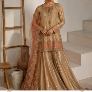 Noor-e-Gulab Champagne Sharara Suit by Maharani Designer Boutique Step into understated luxury with the Noor-e-Gulab Champagne Sharara Suit, an elegant three-piece ethnic ensemble created for women who appreciate refined embroidery, graceful silhouettes and sophisticated colour combinations. Presented by Maharani Designer Boutique, this designer suit beautifully blends a warm champagne-gold kurta and flowing sharara with a soft peach dupatta, creating a polished look for weddings, festive celebrations, engagement parties, receptions and special occasions. The ensemble is designed around a harmonious combination of neutral champagne tones and delicate peach accents. The warm golden-beige kurta provides a sophisticated foundation, while the peach-toned lower border and matching dupatta add softness and feminine contrast. Fine ornamental embroidery is distributed across the neckline, sleeves and lower hem, giving the outfit an elevated festive character without making the overall appearance feel visually overwhelming. The flowing sharara creates dramatic movement with every step, while the embroidered dupatta completes the outfit with an elegant finishing layer. Together, the three pieces create a timeless Indian ethnic look that can be styled traditionally or interpreted in a more contemporary way. Whether you are searching for a designer sharara suit, champagne sharara suit, party wear sharara suit, wedding guest outfit, embroidered Punjabi suit, or an elegant ethnic ensemble for a special celebration, Noor-e-Gulab offers a sophisticated option from Maharani Designer Boutique. A Sophisticated Champagne-Gold Colour Palette The most striking feature of Noor-e-Gulab is its warm champagne-gold colour palette. Champagne is a particularly elegant choice for occasion wear because it provides the richness associated with traditional gold while maintaining a softer, more contemporary appearance. The kurta and sharara share a coordinated champagne-gold tone, creating a beautifully elongated monochromatic base. Against this neutral foundation, the peach detailing becomes a subtle highlight. This colour combination works beautifully for both daytime and evening occasions. For daytime celebrations, pair the suit with delicate jewellery and neutral footwear for a graceful appearance. For evening events, introduce statement earrings, embellished heels and a metallic clutch to enhance the luxurious character of the outfit. The overall colour story is sophisticated, feminine and versatile. Embroidered Kurta The kurta is the focal point of the Noor-e-Gulab ensemble. It features a graceful straight silhouette with a rounded neckline and an elegant keyhole-inspired opening detail at the front. The neckline is surrounded by delicate ornamental embroidery that gradually extends downward into the central design. The embroidery incorporates floral and decorative motifs, creating a refined handcrafted-inspired appearance. Small motifs are distributed across the body of the kurta, providing subtle detailing without covering the entire surface. The lower section becomes more elaborate, with a broad embroidered border introducing additional depth and visual richness. This progression—from lighter detailing across the body to more concentrated embroidery near the hem—creates a balanced design. Intricate Neckline Detailing The neckline deserves special attention. A decorative embroidered frame surrounds the neckline and opening, drawing attention toward the face while giving the kurta a distinctive designer finish. The embroidery includes delicate floral-inspired elements and ornamental patterns that complement the champagne-gold base. The central neckline detail creates a vertical visual line that works particularly well with the elongated silhouette of the kurta. This makes the neckline an ideal focal point when styling the outfit with earrings or a necklace. For a minimalist look, pair it with statement earrings and skip the necklace. For a traditional occasion, add a delicate choker or layered jewellery. Beautiful Sleeve Embroidery The long sleeves continue the decorative language of the kurta. Fine embroidery appears across the sleeve cuffs, creating a concentrated border that complements the neckline and hem. This detail becomes particularly attractive when paired with traditional bangles. The sleeves provide a graceful balance between the decorated front of the kurta and the flowing lower silhouette. Their relatively streamlined structure also allows the outfit to retain a sophisticated appearance despite the richness of the embroidery. Decorative Kurta Hem The lower border of the kurta introduces another important design element. A decorative embroidered panel runs across the hem, incorporating floral and ornamental motifs. The border appears in coordinated tones that connect the champagne-gold kurta with the peach accents seen elsewhere in the ensemble. This creates a seamless transition between the upper and lower portions of the outfit. The hem embroidery also provides an attractive finishing point to the kurta, particularly when viewed with the flowing sharara underneath. Flowing Champagne Sharara The sharara is designed to add movement and volume to the ensemble. Its wide, flowing silhouette creates an elegant flare that becomes especially noticeable while walking or moving across a room. The coordinated champagne-gold colour maintains the monochromatic character of the outfit, while the subtle sheen visible in the design adds dimension. The wide-leg silhouette gives the traditional sharara a contemporary feel and allows the outfit to move beautifully. The sharara works particularly well for women who want the visual drama of a traditional festive outfit while maintaining a graceful and fluid silhouette. Peach-Toned Sharara Border The lower edge of the sharara features delicate peach-toned detailing that connects visually with the dupatta. This creates a subtle contrast against the champagne base. Rather than using a strong contrasting colour, the design relies on closely related warm tones, resulting in a sophisticated overall appearance. The border adds definition to the flowing sharara and helps frame the silhouette. It also provides a visual connection between the kurta's embroidered detailing and the peach dupatta. Elegant Peach Dupatta The peach dupatta is one of the most beautiful components of Noor-e-Gulab. Its soft peach tone provides a gentle contrast to the champagne-gold kurta and sharara. The dupatta features delicate embroidery and an elaborate border, giving it an elevated festive appearance. Its graceful drape adds softness to the outfit and creates beautiful movement when carried over the shoulder. The embroidered border frames the dupatta and makes it particularly suitable for traditional styling. It can be draped over one shoulder, carried across both shoulders or styled more traditionally depending on the occasion. Detailed Dupatta Border The dupatta border is richly decorated with floral and ornamental embroidery. This border provides structure to the otherwise lightweight visual appearance of the dupatta. When draped over the shoulder, the embroidered edge becomes a prominent decorative element alongside the kurta. For photographs, allowing the border to fall naturally down the front creates a beautiful vertical line. For a more traditional appearance, the dupatta can be carried across the front or placed over the head. A Perfect Wedding Guest Outfit Noor-e-Gulab is an excellent choice for wedding guests looking for something elegant without appearing overly bridal. Its champagne and peach palette is sophisticated enough for formal celebrations while remaining versatile. Wear it for: Wedding receptions Engagement ceremonies Sangeet celebrations Mehndi functions Family weddings Festive dinners Anniversary celebrations Traditional gatherings Formal parties Cultural events Pre-wedding celebrations The ensemble can easily be adapted according to the formality of the event. Engagement Party Styling For an engagement party, style Noor-e-Gulab with elegant statement earrings and a delicate bracelet. A sleek hairstyle or soft waves can complement the neckline. Choose a small embellished clutch and footwear in gold, champagne or nude tones. For jewellery, consider pearl, gold-toned, kundan-inspired or crystal-style pieces depending on your personal aesthetic. The result is refined and celebratory without competing with the bride-to-be. Reception Look For an evening reception, embrace the luxurious side of the ensemble. Pair the suit with: Statement earrings A delicate necklace or choker Metallic heels Embellished clutch Stacked bangles A polished hairstyle Soft luminous makeup can complement the warm champagne tones beautifully. A deeper peach, rose or nude lip can add definition while maintaining the elegant colour story. Mehndi Function Styling For a mehndi event, you can make the look more playful by introducing colourful accessories. Try: Floral jewellery Colourful bangles Embellished juttis Decorative hair accessories A colourful potli The champagne base acts as a neutral canvas, allowing brighter accessories to become accents. This makes the outfit versatile enough to be styled differently for different functions. Sangeet Styling For a sangeet celebration, style the sharara with a slightly more glamorous approach. Choose statement earrings, metallic footwear and a decorative clutch. Keep the dupatta draped over one shoulder so the sharara remains visible. The wide-leg silhouette creates natural movement, making the outfit particularly attractive for an energetic celebration. A contemporary updo or flowing waves can complete the look. Jewellery Guide Noor-e-Gulab works with several jewellery styles. Gold Jewellery Gold-toned jewellery complements the champagne base and creates a traditional appearance. Pearl Jewellery Pearls introduce softness and work particularly well with the peach dupatta. Kundan-Inspired Jewellery Kundan-style pieces can enhance the traditional character of the outfit. Crystal Jewellery Crystal-inspired jewellery can create a more contemporary evening look. Jhumkas Traditional jhumkas remain one of the easiest ways to style this ensemble. Choker A delicate choker can beautifully frame the neckline. Footwear Recommendations The flowing sharara looks beautiful with footwear that complements its graceful movement. For traditional occasions, choose embellished Punjabi juttis or mojaris. For formal evening functions, consider metallic sandals or heels. Nude and champagne footwear can create a seamless elongated appearance. Gold-toned footwear is another natural pairing with the warm colour palette. When selecting footwear, prioritize comfort if you expect to wear the outfit for several hours. Dupatta Draping Ideas Classic Shoulder Drape Place the dupatta over one shoulder and allow the embroidered edge to fall vertically. Two-Shoulder Drape Carry the dupatta across both shoulders for a balanced traditional appearance. Front Drape Bring the dupatta across the front for a more modest and classic look. Head Drape For traditional ceremonies, the dupatta can be gracefully placed over the head. Contemporary Drape Allow the dupatta to fall loosely from one shoulder for a relaxed designer look. Hairstyle Ideas The neckline and embroidery provide plenty of styling possibilities. Low Bun A sleek low bun creates a sophisticated formal appearance. Soft Waves Loose waves offer a feminine and contemporary finish. Side-Swept Waves A side-swept hairstyle can highlight statement earrings. Braided Style A decorated braid creates a traditional Indian aesthetic. Sleek Ponytail A sleek ponytail gives the outfit a modern fashion-forward character. Makeup Inspiration The warm colour palette allows for both subtle and glamorous makeup. For daytime events, choose luminous skin, soft brown eye makeup, defined lashes and a peach or nude lip. For evening celebrations, add more defined eyeliner, a glowing complexion and a deeper rose or warm nude lip. Peach-toned blush can complement the dupatta while maintaining a harmonious colour palette. The objective is to enhance the outfit rather than compete with its embroidery. Versatile Ethnic Fashion One of the biggest advantages of Noor-e-Gulab is its versatility. Although designed as a coordinated occasion ensemble, its individual elements can inspire multiple looks. The kurta can be styled with contrasting palazzos or straight pants. The sharara can be paired with another coordinated ethnic top for a new outfit combination. The peach dupatta can complement other champagne, beige, peach, blush or pastel outfits. This allows the pieces to become part of a broader ethnic wardrobe. Contemporary Indian Elegance Modern Indian fashion increasingly combines traditional silhouettes with refined contemporary styling. Noor-e-Gulab reflects this approach through its combination of: Traditional sharara silhouette Long embroidered kurta Soft contrasting dupatta Elegant neutral colour palette Feminine embroidery Flowing proportions Contemporary styling potential The result is an outfit that feels rooted in Indian ethnic fashion while remaining suitable for modern celebrations. Why Choose Noor-e-Gulab? Choose this designer sharara suit if you are looking for: A sophisticated champagne-gold ethnic outfit A soft peach and gold colour combination An embroidered sharara suit for women A wedding guest outfit A party wear sharara set An elegant engagement outfit A festive designer suit A flowing traditional silhouette A coordinated three-piece ensemble A versatile outfit from Maharani Designer Boutique Noor-e-Gulab is designed to make an impression through colour harmony, embroidery and graceful movement rather than relying solely on heavy embellishment. Styling for Different Occasions The beauty of this outfit lies in how easily its personality can change through accessories. For a daytime family gathering, choose minimal earrings, simple footwear and natural makeup. For a wedding ceremony, introduce traditional jewellery, bangles and embellished footwear. For an evening reception, select statement earrings, a metallic clutch and heels. For an engagement party, combine refined jewellery with a polished hairstyle. For a festive celebration, colourful bangles and traditional juttis can add personality. A Sophisticated Choice for Festive Wardrobes Every occasion-wear wardrobe benefits from a versatile neutral-toned outfit. While bright red, pink and green outfits make strong statements, champagne-gold offers a softer alternative. It is elegant without being overpowering and can be styled with a wide variety of jewellery colours. Peach adds another layer of softness, making the ensemble especially suitable for women who prefer feminine pastel-inspired combinations. Maharani Designer Boutique Maharani Designer Boutique presents ethnic occasion wear that celebrates traditional Indian silhouettes through sophisticated colours and decorative detailing. The Noor-e-Gulab Sharara Suit reflects this design philosophy through its carefully coordinated three-piece composition. The champagne-gold kurta establishes the foundation. The embroidered neckline, sleeves and hem provide decorative character. The flowing sharara introduces movement. The peach dupatta adds softness and contrast. Together, these details create an elegant outfit suitable for celebrations where you want to look polished, feminine and effortlessly stylish. Product Details Product Name: Noor-e-Gulab Champagne Sharara Suit Brand: Maharani Designer Boutique Category: Designer Sharara Suit / Party Wear Suit Primary Colour: Champagne Gold Secondary Colour: Peach Set Includes: Kurta, Sharara and Dupatta Kurta Style: Long embroidered kurta with decorative neckline Bottom Style: Flowing wide-leg sharara Dupatta: Peach-toned embroidered dupatta with decorative border Design: Floral and ornamental embroidery Occasions: Weddings, Engagements, Receptions, Mehndi, Sangeet, Festive Events, Parties and Family Celebrations Exact fabric composition, measurements, lining, embroidery technique and customization availability should be confirmed with Maharani Designer Boutique before purchase, as these specifications cannot be reliably determined from the image alone. Care & Storage To preserve the appearance of an embellished occasion-wear outfit, handle the ensemble carefully. Store the kurta, sharara and dupatta in a clean garment bag away from excessive moisture and direct sunlight. Keep jewellery, sharp accessories and rough surfaces away from the embroidered sections to reduce the possibility of snagging. Avoid applying perfume or cosmetic products directly onto the garment. Follow the garment's specific care label for cleaning and maintenance. Professional cleaning may be appropriate depending on the actual fabric and embellishment. Fold or hang the dupatta carefully so that the embroidered border is not crushed beneath heavy garments. With thoughtful storage and careful handling, the outfit can remain a beautiful part of your occasion-wear wardrobe for future celebrations. champagne sharara suit, champagne gold sharara suit, champagne sharara suit for women, designer sharara suit, designer sharara suit for women, embroidered sharara suit, embroidered sharara suit for women, peach dupatta sharara suit, champagne gold suit, champagne gold ethnic wear, peach and gold suit, peach and gold sharara suit, designer party wear suit, party wear sharara suit, wedding guest sharara suit, wedding guest outfit for women, sharara suit for wedding, sharara suit for engagement, engagement outfit for women, engagement sharara suit, reception outfit for women, reception sharara suit, mehndi outfit for women, mehndi sharara suit, sangeet outfit for women, sangeet sharara suit, festive sharara suit, festive ethnic wear, Indian sharara suit, Indian ethnic wear for women, traditional sharara suit, modern sharara suit, stylish sharara suit, embroidered ethnic suit, designer ethnic wear, ethnic wear for wedding, wedding wear for women, Indian party wear, party wear ethnic suit, embroidered party wear suit, luxury sharara suit, elegant sharara suit, gold embroidered suit, champagne embroidered suit