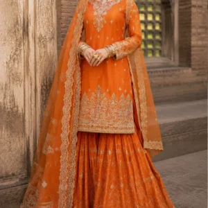 Orange Embroidered Sharara Suit Celebrate the beauty of traditional Indian fashion with Orange Embroidered Sharara Suit, a luxurious orange embroidered sharara suit designed for women who love vibrant colours, intricate craftsmanship, and timeless festive elegance. This stunning ensemble features a rich orange straight-cut kurta, a beautifully flared sharara, and a sheer matching dupatta adorned with elaborate embroidery. The entire outfit is brought together with intricate ivory and antique-gold-toned detailing, creating a regal appearance that beautifully blends traditional Indian aesthetics with contemporary styling. The vibrant orange colour gives the outfit warmth, energy, and festive character, while the delicate embroidery adds sophistication. From the ornate neckline and sleeves to the heavily embroidered kurta hem, patterned sharara, and statement dupatta border, every element contributes to a complete occasion-wear look. The design is particularly suited to weddings, mehendi celebrations, sangeet functions, festive gatherings, engagement ceremonies, family celebrations, and traditional events. With its graceful silhouette and statement detailing, Noor-e-Narangi is created for the woman who wants to make an elegant impression while embracing the richness of Indian craftsmanship. A Vibrant Orange Colour for Festive Celebrations The defining feature of this ensemble is its beautiful orange colour. Orange has a special place in Indian festive fashion. It represents warmth, celebration, energy, and vibrancy, making it an excellent choice for weddings and cultural occasions. The orange base of this outfit creates an eye-catching appearance without relying on excessive embellishment. Instead, the colour itself provides richness, while the intricate ivory and gold-toned embroidery adds refinement. This makes the ensemble particularly suitable for women who enjoy colourful ethnic wear and want an outfit that stands out naturally. The colour can work beautifully for daytime and evening functions. Under natural daylight, the orange creates a fresh and vibrant appearance, while warm evening lighting brings out its deeper and more luxurious character. Intricate Embroidered Kurta The straight-cut kurta forms the elegant upper layer of the outfit. Its silhouette is streamlined and graceful, allowing the detailed embroidery to remain the focus. The neckline features intricate ornamental embroidery that extends down the front, creating a beautifully defined centre panel. Small motifs are distributed across the body of the kurta, adding delicate detail without making the entire surface appear excessively heavy. The sleeves are also decorated with intricate embroidery, creating continuity between the neckline, body, and cuffs. One of the most striking elements is the richly embroidered hem. The lower border features elaborate floral and traditional-inspired patterns arranged in multiple layers. This heavily detailed hem creates a beautiful transition between the kurta and the flared sharara underneath. The result is a sophisticated silhouette that combines the elegance of a long embroidered kurta with the traditional drama of a sharara. Beautifully Flared Sharara The sharara is an important element of this ensemble and gives the outfit its distinctive traditional character. The wide flare creates graceful movement and volume, making the outfit particularly attractive when walking, posing, or participating in celebrations. The orange sharara features an intricate all-over embroidered pattern arranged in delicate geometric and floral-inspired formations. Fine lines create a beautiful lattice-like appearance across the fabric, while smaller motifs add detail throughout the flare. The hem is finished with a wide embroidered border that complements the kurta and dupatta. This coordinated border creates visual balance and gives the sharara a beautifully finished appearance. The flowing flare is particularly suited to festive occasions because it creates movement and dimension while maintaining a graceful silhouette. Statement Sheer Dupatta The matching orange dupatta completes the ensemble and adds an additional layer of sophistication. The sheer-looking fabric allows the orange base to remain visible while the intricate embroidery creates a delicate yet luxurious appearance. One of the most prominent features is the elaborate embroidered border running along the length of the dupatta. The border features multiple layers of ornamental detailing, giving it a beautifully defined edge. Additional embroidered motifs are distributed across the body of the dupatta, creating visual continuity with the kurta and sharara. The dupatta can be styled traditionally over the head, draped across one shoulder, or arranged around the arms for a more contemporary appearance. For a wedding or mehendi function, wearing the dupatta over the head creates a graceful traditional look. For a reception or evening event, a shoulder drape can highlight the embroidery and neckline more effectively. Traditional Embroidery with a Contemporary Silhouette One of the most appealing aspects of this ensemble is the balance between traditional detailing and contemporary styling. The embroidery draws inspiration from classic Indian textile aesthetics, while the straight-cut kurta and flowing sharara create a polished modern silhouette. This combination makes the outfit versatile for women of different ages and styling preferences. You can accessorise it traditionally with a statement necklace, jhumkas, bangles, and a maang tikka, or create a contemporary look with statement earrings, a sleek clutch, and minimal jewellery. The outfit itself provides enough detailing to support both styling directions. Perfect for Mehendi Celebrations The vibrant orange shade makes this ensemble particularly suitable for mehendi celebrations. Mehendi functions are traditionally associated with bright, cheerful colours, and orange creates an energetic festive appearance. Pair the outfit with colourful bangles, floral jewellery, statement earrings, and soft waves for a playful mehendi look. For a more sophisticated interpretation, choose gold-toned jewellery and a sleek hairstyle. The flowing sharara also provides excellent movement, making it suitable for celebrations involving dancing and social gatherings. Beautiful Sangeet Outfit The sharara silhouette makes Noor-e-Narangi an excellent choice for a sangeet. The flare moves beautifully while walking and dancing, giving the outfit a dynamic appearance. For a glamorous sangeet styling, pair it with oversized earrings, a sleek bun or soft waves, and a metallic clutch. You can also add traditional bangles for a more festive appearance. The dupatta can be secured over one shoulder to allow greater freedom of movement while keeping the embroidered border visible. Ideal for Weddings This orange embroidered sharara suit is suitable for a wide range of wedding functions. It can be worn by the bride for a pre-wedding celebration, by a bridesmaid, by the bride's sister, or by a wedding guest looking for an elegant traditional outfit. The colour makes it particularly suitable for daytime ceremonies and vibrant pre-wedding events, while the embroidery gives it enough richness for evening celebrations. Suitable occasions include: Mehendi ceremonies Sangeet functions Engagement celebrations Wedding receptions Family weddings Festive gatherings Diwali celebrations Traditional ceremonies Destination weddings Wedding guest events Cultural celebrations Formal family occasions Elegant Engagement Wear For an engagement ceremony, this ensemble can be styled with refined jewellery and a sophisticated beauty look. A statement choker paired with matching earrings can beautifully frame the embroidered neckline. Alternatively, choose large earrings and leave the neck free to create a more contemporary appearance. A soft bun decorated with flowers can introduce a traditional touch, while loose waves create a modern romantic look. The vibrant orange colour photographs beautifully, making the outfit a strong choice for engagement portraits. Festive Indian Wear Orange has an inherently festive quality, making this ensemble suitable for celebrations beyond weddings. Wear it for Diwali gatherings, family celebrations, cultural events, festive dinners, anniversary parties, and other traditional occasions. The detailed embroidery ensures that the outfit feels special enough for formal events, while the sharara silhouette gives it a youthful and contemporary character. It can easily become a versatile addition to an Indian festive wardrobe. Jewellery Styling The ivory and gold-toned embroidery creates numerous jewellery possibilities. For a traditional appearance, choose gold-toned jewellery with intricate detailing. Kundan-inspired jewellery can complement the ornate Indian character of the outfit beautifully. For a lighter look, choose pearl or polki-inspired earrings. For a modern celebration, oversized statement earrings can create an elegant appearance without requiring a heavy necklace. Traditional bangles are another natural choice. You can mix gold-toned bangles with orange or complementary shades to create a festive stack. For bridal-inspired styling, add a maang tikka and traditional earrings. Hairstyle Suggestions A centre-parted low bun is a timeless choice for this ensemble. It creates a polished appearance and provides an excellent foundation for traditional jewellery. For mehendi or sangeet functions, soft waves can create a more relaxed and youthful appearance. A braided hairstyle decorated with flowers can also complement the traditional character of the outfit. If the dupatta is worn over the head, a neat bun helps maintain a clean and elegant silhouette. For a contemporary reception look, sleek straight hair or soft waves can create a sophisticated contrast with the traditional embroidery. Makeup Styling The vibrant orange colour works beautifully with warm and luminous makeup. For daytime functions, choose natural-looking skin, softly defined eyes, warm blush, and a nude or peach-toned lip. For evening celebrations, you can add gold or bronze eyeshadow, stronger eyeliner, and a deeper rose or terracotta lip. Warm-toned makeup complements the orange fabric particularly well. A subtle glow on the cheekbones can also enhance the overall festive appearance. The goal should be to create balance so that the embroidery and colour remain the primary focus. Traditional Dupatta Draping The sheer dupatta provides several styling possibilities. For a traditional Indian appearance, place the dupatta over the head and allow both embroidered borders to frame the body. For a more contemporary appearance, drape it over one shoulder and let it fall naturally. You can also arrange the dupatta around both arms for a graceful formal look. The ornate border becomes especially prominent when the dupatta is styled over the shoulder, making this option ideal for photographs. Photography-Friendly Design The rich orange colour and elaborate embroidery make this ensemble particularly attractive in photographs. The kurta provides structured detailing around the neckline and hem, while the sharara creates movement and volume. The dupatta adds another layer of texture and allows the embroidered border to create a strong visual frame. The combination of orange and ivory-gold detailing also creates a beautiful contrast against heritage architecture, neutral backgrounds, garden settings, and traditional wedding décor. This makes the outfit especially suitable for wedding photography, engagement portraits, family photographs, and festive photoshoots. A Graceful Outfit for the Modern Indian Woman Contemporary Indian fashion is increasingly about combining heritage-inspired craftsmanship with practical, wearable silhouettes. This outfit reflects that approach. The straight-cut kurta offers a polished appearance, while the sharara introduces traditional volume and movement. The embroidery provides the grandeur associated with occasion wear without requiring an extremely heavy silhouette. This balance makes the ensemble suitable for women who want traditional Indian fashion with a contemporary sense of styling. Wedding Guest Styling As a wedding guest, you can create a sophisticated look by keeping your accessories balanced. Choose statement earrings, a sleek clutch, and elegant footwear. Allow the embroidery to remain the focal point rather than adding too many competing accessories. For a close family wedding, you can increase the jewellery and add a traditional maang tikka. For a formal reception, choose metallic heels and a structured clutch for a polished finish. The versatility of the outfit makes it suitable for different wedding roles. Destination Wedding Appeal The vibrant orange colour can create a striking look at destination weddings. Whether the celebration takes place in a heritage palace, luxury resort, traditional haveli, garden venue, or outdoor location, the colour and embroidery can complement the surroundings beautifully. The flowing sharara creates movement in photographs, while the sheer dupatta adds softness. For destination weddings, consider lightweight jewellery and comfortable footwear while allowing the outfit itself to remain the statement piece. Custom-Made Designer Wear At Maharani Designer Boutique, selected outfits can be made to measure or customised according to individual requirements, subject to the design. Customers can discuss measurements, preferred fitting, neckline preferences, sleeve requirements, dupatta styling, and other possible customisation details. For customers ordering for a specific event, it is recommended to share the event date before confirming the order. This allows the appropriate production timeline to be discussed. Detailed embroidered outfits require careful construction and finishing, so production time can vary depending on the final specifications. Premium Indian Occasion Wear A beautifully designed ethnic outfit should combine colour, craftsmanship, silhouette, and finishing. This ensemble brings these elements together through its vibrant orange base, intricate embroidery, flowing sharara, and statement dupatta. The design is elaborate without appearing visually chaotic. The embroidery is carefully distributed across the outfit, creating areas of detailed focus while allowing the orange fabric to remain visible. This balance helps the outfit retain its elegance despite its rich embellishment. Suitable for International Celebrations Indian weddings and festive occasions are celebrated across the globe, and vibrant designer ethnic wear remains an important part of these celebrations. This orange sharara suit can be styled for Indian weddings and cultural events in Canada, the USA, the UK, Australia, New Zealand, and other international destinations. Its traditional character makes it especially appropriate for weddings where Indian heritage and contemporary fashion come together. Maharani Designer Boutique offers PAN India and worldwide shipping options for customers seeking designer Indian occasion wear. Care and Storage Due to the detailed embroidery and delicate dupatta, careful handling is recommended. Store the outfit in a clean, dry garment bag when not in use. Avoid placing heavy objects directly on embroidered sections. The dupatta should be folded carefully to help protect its detailed border. Professional cleaning is recommended for heavily embellished occasion wear, with the final cleaning method determined according to the actual fabric and embroidery used. Always follow the garment's specific care instructions. Why Choose Noor-e-Narangi? Choose Noor-e-Narangi if you are looking for: A vibrant orange designer sharara suit Traditional Indian embroidery A statement wedding outfit A mehendi or sangeet ensemble A festive sharara suit An elegant wedding guest outfit A richly embroidered kurta A flowing flared sharara A statement sheer dupatta Traditional-inspired occasion wear Custom-made Indian clothing Designer ethnic wear Premium festive fashion A Timeless Festive Investment The appeal of this ensemble extends beyond a single occasion. Its traditional silhouette and vibrant colour allow it to remain relevant across different celebrations. The orange shade makes it ideal for festive seasons, while the classic embroidery gives the outfit a timeless character. With different jewellery and styling choices, the ensemble can create multiple looks. For one occasion, it can feel traditional and regal. For another, it can appear contemporary and glamorous. For a family celebration, it can be styled more subtly. For a wedding, it can become a statement ensemble. Final Look Noor-e-Narangi is a celebration of vibrant Indian fashion, intricate embroidery, and graceful traditional styling. The rich orange kurta provides a striking foundation, while the ornate ivory and gold-toned embroidery adds sophistication. The flowing sharara creates volume and movement, and its elaborate hem complements the detailed kurta border. The sheer embroidered dupatta completes the ensemble with a beautifully ornate border and scattered motifs, adding elegance and dimension. Whether you are attending a mehendi, sangeet, engagement, wedding reception, festive celebration, or another special occasion, this orange embroidered sharara suit offers a sophisticated way to embrace traditional Indian fashion. Discover designer Indian occasion wear at Maharani Designer Boutique, where timeless craftsmanship meets contemporary styling. For current availability, pricing, fabric details, measurements, customisation, production timelines, and shipping information, contact the boutique directly before placing your order. Maharani Designer Boutique Jalandhar, Punjab, India PAN India & Worldwide Shipping Product Highlights Vibrant orange designer sharara suit Straight-cut embroidered kurta Intricate ivory and gold-toned embroidery Detailed embroidered neckline Embellished full sleeves Heavy embroidered kurta hem Flowing flared sharara All-over patterned sharara embroidery Detailed sharara border Sheer orange embroidered dupatta Ornate dupatta border Traditional-inspired floral and ornamental motifs Ideal for mehendi and sangeet Perfect for weddings and festive celebrations Suitable for engagement ceremonies Elegant wedding guest outfit Customisation may be available PAN India and worldwide shipping Orange sharara suit, orange designer sharara suit, orange sharara suit online, orange embroidered suit, orange wedding suit, orange wedding outfit, orange ethnic wear, designer sharara suit, designer sharara online, embroidered sharara suit, wedding sharara suit, wedding guest sharara, mehendi sharara suit, sangeet sharara suit, engagement sharara suit, festive sharara suit, orange festive wear, orange Indian suit, orange Punjabi suit, designer ethnic wear, Indian designer suit, embroidered kurta sharara, sharara with dupatta, designer suit with dupatta, wedding wear for women, luxury Indian clothing, boutique suits online, designer boutique suits, boutique suits in Jalandhar, Indian clothing boutique, Maharani Designer Boutique.