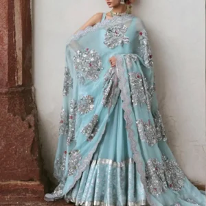 Pastel Aqua Blue Anarkali Gown – A Dreamy Expression of Contemporary Indian Couture Make a graceful statement at your next celebration with this Pastel Aqua Blue Anarkali Gown with Silver Floral Embroidery, an exquisite designer ensemble created for women who love soft pastel colours, luxurious embellishment, flowing silhouettes, and elegant Indian craftsmanship. The outfit features a beautiful pastel aqua blue base adorned with intricate silver-toned floral embroidery and shimmering embellishment. Delicate hints of pink and red add subtle colour to the floral motifs, creating a sophisticated contrast against the cool blue background. The flowing Anarkali-style silhouette gives the outfit a graceful fall, while the richly decorated lower section adds volume, texture, and movement. A beautifully coordinated sheer dupatta completes the ensemble. Covered with ornate floral motifs and finished with a scalloped embroidered border, the dupatta creates an elegant layered effect and adds a luxurious finishing touch to the outfit. This designer Anarkali suit is an ideal choice for weddings, engagement ceremonies, receptions, sangeet celebrations, festive gatherings, formal dinners, destination weddings, and other special occasions where you want your outfit to feel sophisticated and memorable. The combination of pastel aqua blue, silver embroidery, floral detailing, and a dramatic flowing silhouette creates a look that feels both traditional and contemporary. A Beautiful Pastel Aqua Blue Colour The soft aqua blue shade gives this outfit its distinctive personality. Pastel blue has become a favourite in contemporary Indian occasion wear because it offers a refreshing alternative to conventional reds, maroons, oranges, and jewel tones. It creates a softer and more sophisticated appearance while still allowing elaborate embroidery and embellishment to take centre stage. In this design, the aqua blue base provides a serene canvas for the silver floral embroidery. The cool blue tone allows the metallic detailing to appear luminous, while tiny pink and red accents add warmth to selected floral motifs. The resulting colour palette feels elegant, feminine, and refined. It is especially suited to women who want an occasion outfit that feels luxurious without appearing excessively heavy in colour. The pastel shade also photographs beautifully, making this ensemble an excellent choice for wedding photography, engagement portraits, family photographs, and festive celebrations. Intricate Silver Floral Embroidery The defining feature of this Anarkali ensemble is its elaborate floral embroidery. Large floral motifs are carefully positioned across the front of the outfit, creating eye-catching focal points. Smaller floral details and ornamental patterns extend across different sections, giving the garment a beautifully layered appearance. The silver-toned embellishment creates a subtle shimmer against the pastel aqua blue background. The floral motifs are not limited to one section of the garment. They continue across the bodice, flowing skirt, sleeves, and dupatta, creating a coordinated visual story throughout the entire ensemble. This continuity gives the outfit a couture-inspired appearance. The silver detailing can catch the light beautifully as the wearer moves, creating a soft luminous effect that is particularly attractive for evening events. Graceful Anarkali Silhouette The flowing Anarkali-inspired silhouette creates one of the most elegant features of the ensemble. The bodice follows a structured form before opening into a generous flare. The lower portion spreads gracefully around the body, creating movement and volume without compromising the feminine shape of the outfit. The silhouette is particularly beautiful when walking because the fabric moves naturally with every step. The flare also allows the embroidered details to become visible from different angles. For wedding entrances, receptions, photographs, and formal celebrations, a flowing Anarkali silhouette can create a dramatic yet graceful appearance. The design balances traditional Indian dressing with a contemporary sense of proportion, making it suitable for women who want the elegance of a traditional ensemble with a modern finish. Beautifully Detailed Lower Section The lower section of the Anarkali is richly detailed with patterned embroidery and a statement metallic-toned hem. The flared portion appears to feature intricate repeating patterns that add depth to the pastel blue base. Near the hem, the design becomes more elaborate, creating a stronger visual finish. The metallic border defines the bottom of the garment and gives the flowing silhouette structure. As the wearer moves, the border creates a beautiful visual rhythm around the flare. This combination of detailed fabric, embroidery, and a defined hem makes the lower portion particularly attractive in full-length photographs. The flare also creates a regal effect when the outfit is spread or photographed while walking. Statement Sheer Dupatta The dupatta adds another layer of elegance to this ensemble. Designed in a lightweight, sheer-looking pastel aqua blue fabric, it allows the colour of the outfit underneath to remain visible while introducing additional embroidery and embellishment. Large floral motifs decorate the dupatta, creating continuity with the main Anarkali. The border is one of the most striking features. A delicate scalloped edge runs along the perimeter, decorated with intricate silver-toned embroidery. The scalloped finish creates a softer and more feminine appearance than a straight border. The dupatta can be draped over one shoulder, arranged across both arms, or styled over the head for a more traditional Indian appearance. For bridal or wedding ceremonies, wearing the dupatta over the head can create a graceful and ceremonial look. For a reception or cocktail-style celebration, draping it over one shoulder can create a more contemporary silhouette. Floral Motifs with Subtle Colour Accents The floral motifs are primarily silver and metallic in appearance, but subtle touches of pink and red can be seen within selected embellishments. These small colour accents are important because they prevent the silver detailing from appearing too monochromatic. The soft pink tones complement the aqua blue beautifully, while the occasional deeper accents create visual depth. The floral arrangement gives the outfit a romantic personality while maintaining the grandeur expected from designer occasion wear. The result is a design that feels feminine without becoming overly delicate. Perfect for Weddings This pastel blue designer Anarkali is a beautiful option for wedding celebrations. Its soft colour palette makes it suitable for a range of wedding functions, while the intricate embroidery provides enough richness for formal occasions. It can be styled for: Wedding receptions Engagement ceremonies Sangeet celebrations Mehendi functions Family weddings Cocktail evenings Festive celebrations Destination weddings Formal dinners Anniversary celebrations Cultural events Wedding guest dressing Pre-wedding celebrations For a daytime wedding, pair it with delicate jewellery and soft makeup. For an evening reception, add statement earrings, a glamorous clutch, and more defined makeup. The outfit can therefore be adapted to suit the mood and timing of the celebration. Elegant Engagement Outfit Engagement ceremonies are ideal occasions for pastel colours. This aqua blue Anarkali provides a sophisticated alternative to traditional engagement outfits in darker shades. The colour feels fresh and celebratory, while the silver embellishment provides enough glamour for photographs and formal festivities. Pair the outfit with a statement choker, elegant earrings, soft curls, and luminous makeup for a romantic engagement look. For a more contemporary appearance, wear statement earrings without a necklace. This keeps the neckline visible and allows the embroidery to become the focal point. A delicate maang tikka can also be added for a more traditional Indian styling. Perfect for Reception Wear The intricate embroidery and shimmering detailing make this ensemble especially appropriate for a wedding reception. Reception events often call for outfits that feel glamorous while remaining elegant. The flowing silhouette creates a sophisticated evening appearance, while the pastel colour keeps the outfit from appearing overly heavy. For a reception, style the ensemble with: Statement earrings A delicate or statement necklace Metallic clutch Embellished footwear Soft waves or a sleek bun Luminous makeup Subtle highlighter The silver embellishment will naturally complement metallic accessories and evening lighting. Beautiful Sangeet Styling The flowing silhouette makes this ensemble suitable for sangeet celebrations. The flare provides movement, making the outfit visually appealing while walking, posing, and dancing. For a sangeet, the dupatta can be secured neatly over one shoulder or arranged around the arms so that the wearer can move comfortably. Statement earrings and a sleek hairstyle can create a modern party look. Alternatively, traditional jewellery and bangles can give the outfit a more classic Indian character. The versatility of the silhouette allows the styling to change according to personal preference. Festive Indian Wear with a Modern Touch This ensemble demonstrates how Indian occasion wear can incorporate traditional detailing while maintaining a contemporary colour palette. The Anarkali silhouette is deeply rooted in Indian fashion, but the pastel aqua blue colour and silver embellishment give the design a modern identity. It is suitable for women who appreciate traditional craftsmanship but prefer lighter, fresher colours. The outfit can be worn for festive celebrations, family gatherings, cultural occasions, formal dinners, and special celebrations. Its sophisticated colour palette also makes it suitable for women who prefer understated luxury. Jewellery Styling The cool pastel blue and silver colour combination creates many jewellery possibilities. For a traditional Indian appearance, pair the outfit with a silver-toned, diamond-inspired, or crystal jewellery set. Pearl jewellery can also complement the soft pastel palette beautifully. For a more traditional wedding appearance, choose jewellery featuring silver, white stones, pearls, or subtle pastel accents. For a modern reception, large statement earrings may be enough. A choker can beautifully frame the neckline, while a longer necklace can add another layer of elegance. Bangles can be selected in silver, crystal, pearl, or complementary pastel shades. The jewellery should ideally complement rather than compete with the elaborate floral embroidery. Hairstyle Suggestions A sleek low bun is a timeless option for this Anarkali. It keeps the neckline and jewellery visible and creates a polished formal appearance. For a traditional wedding look, a centre-parted bun decorated with flowers can beautifully complement the pastel colour palette. For an engagement or reception, soft waves can create a more contemporary and romantic appearance. Loose curls can also work beautifully with the flowing silhouette. If the dupatta is worn over the head, a neat bun becomes particularly practical and elegant. Makeup Suggestions The pastel aqua blue shade works beautifully with luminous makeup. For daytime celebrations, choose fresh skin, softly defined eyes, rosy cheeks, and a nude-pink or soft rose lip. For evening functions, add subtle shimmer to the eyes and more defined eyeliner. Silver or champagne-toned eyeshadow can complement the embroidery without overpowering the outfit. A soft pink, mauve, rose, or berry-toned lip can work beautifully depending on the desired intensity. The overall makeup should maintain balance between the soft colour palette and the statement embroidery. Destination Wedding Style Pastel colours are particularly attractive for destination weddings. This aqua blue Anarkali can create an elegant appearance against heritage architecture, palace-inspired venues, luxury hotels, gardens, and outdoor wedding locations. The flowing silhouette photographs beautifully against architectural backgrounds. The sheer embroidered dupatta can also create movement in outdoor photographs, especially when styled over one shoulder or allowed to flow naturally. For a destination wedding, pair the outfit with lightweight statement jewellery and a structured clutch. Photography-Friendly Design A special occasion outfit should look beautiful from every angle. This design contains several elements that create visual interest in photographs. The large floral motifs provide close-up details. The flowing flare creates movement in full-length photographs. The metallic border defines the lower silhouette. The sheer dupatta adds depth and transparency. The scalloped embroidered border provides an elegant frame. The pastel aqua blue colour creates a soft visual contrast against traditional architecture, neutral interiors, gardens, and wedding décor. Together, these elements make the outfit particularly suitable for photography. A Feminine and Sophisticated Silhouette The overall design is feminine without being excessively ornate in colour. The pastel base keeps the outfit visually soft, while the extensive silver embellishment provides the required richness. The flowing skirt-like lower portion creates a graceful silhouette, while the fitted upper section gives the outfit structure. This balance allows the ensemble to feel elegant and comfortable while maintaining the grandeur of designer occasion wear. Suitable for Wedding Guests Although the design has a luxurious bridal-inspired aesthetic, it can also be styled beautifully as a wedding guest outfit. For a wedding guest, keep the jewellery slightly lighter and allow the embroidery to remain the focus. A statement earring, elegant clutch, soft hairstyle, and refined makeup can create a polished appearance. For close family members, the jewellery can be increased to create a more elaborate festive look. This versatility makes the ensemble suitable for different roles within a wedding celebration. Contemporary Indian Couture Indian couture is increasingly influenced by a combination of traditional craftsmanship and modern styling. This ensemble reflects that approach through its traditional Anarkali silhouette, floral embroidery, embellished dupatta, and metallic detailing, while the pastel aqua blue palette provides a contemporary aesthetic. It is ideal for women who want their Indian clothing to feel luxurious but not overly traditional. The design can be styled traditionally with classic jewellery or modernised through contemporary accessories. Custom-Made Designer Experience At Maharani Designer Boutique, selected designer outfits can be developed with individual measurements and styling preferences in mind. For made-to-order or customised versions, customers can discuss fitting requirements, measurements, neckline preferences, sleeve styling, dupatta arrangement, and other design considerations where applicable. Customers ordering for a specific wedding or celebration are encouraged to share their event date in advance. This allows the appropriate production timeline to be discussed before confirming the order. Because detailed occasion wear requires careful embroidery, finishing, and construction, production timelines may vary depending on the design and level of customisation. Ideal for Women Who Love Pastel Luxury Pastel luxury is about combining soft colours with refined craftsmanship. This outfit is perfect for women who want an elegant colour palette without sacrificing intricate detailing. The aqua blue base creates softness. The silver embroidery adds glamour. The floral motifs create romance. The flowing silhouette adds grace. The embellished dupatta provides drama. The overall effect is luxurious, feminine, and sophisticated. Styling for Different Occasions The versatility of this Anarkali allows you to create different looks through accessories. For an engagement, pair it with delicate jewellery and soft curls. For a sangeet, choose statement earrings and a contemporary hairstyle. For a reception, add a statement necklace, metallic clutch, and glamorous makeup. For a festive celebration, choose traditional jewellery and bangles. For a daytime wedding, keep the accessories light and let the pastel colour shine. This adaptability makes the ensemble a beautiful investment for an occasion-wear wardrobe. Indian Wear for Global Celebrations Indian weddings and celebrations are enjoyed across the world, and pastel designer outfits have become increasingly popular among women looking for elegant ethnic wear outside India. This ensemble can be styled for Indian weddings, receptions, engagement celebrations, Diwali gatherings, cultural events, and family functions in India as well as international destinations. Maharani Designer Boutique caters to customers seeking premium Indian occasion wear with PAN India and worldwide shipping options. Whether you are shopping from Jalandhar or preparing for a wedding abroad, you can discuss measurements, availability, customisation, and delivery requirements with the boutique. Care and Storage Because this outfit features detailed embroidery and embellishment, careful handling is recommended. Store the ensemble in a clean and dry garment bag when not in use. Avoid placing heavy objects directly over embroidered sections. The dupatta should be folded or stored carefully to help protect its embroidered border and decorative motifs. For cleaning, follow the care instructions appropriate to the actual fabric and embellishments used in the finished garment. Professional cleaning is recommended for heavily embellished occasion wear. Why Choose This Designer Anarkali? This ensemble is an excellent choice if you are searching for: A pastel blue designer Anarkali A luxury Indian occasion outfit An embroidered Anarkali suit A wedding guest outfit An engagement outfit A reception outfit A sangeet outfit A festive Indian outfit A pastel wedding outfit A floral embroidered suit A designer Anarkali with dupatta A custom-made Indian outfit Premium ethnic wear Contemporary Indian couture A Timeless Occasion-Wear Investment Trends may change, but elegant Indian silhouettes remain timeless. The Anarkali has continued to evolve across generations because of its ability to create a graceful, feminine silhouette while offering endless opportunities for embroidery, colour, and styling. This pastel aqua blue version gives the classic silhouette a contemporary personality. The soft colour makes it suitable for multiple occasions, while the intricate embroidery ensures that it remains a statement piece. It can become part of your festive wardrobe for weddings, receptions, engagement celebrations, and other important events. Final Look This Pastel Aqua Blue Anarkali Gown with Silver Floral Embroidery and Embellished Dupatta is a celebration of elegance, craftsmanship, colour, and movement. The soft aqua blue base creates an ethereal appearance, while the intricate silver floral embellishment adds luxury and sophistication. Subtle pink and red accents give the floral motifs additional depth. The flowing Anarkali silhouette creates graceful movement, while the richly decorated lower section and metallic-toned hem provide structure. The embroidered sheer dupatta completes the outfit with statement floral motifs and a beautifully scalloped border. Whether you are attending a wedding reception, engagement, sangeet, festive celebration, destination wedding, or formal family occasion, this designer ensemble offers an elegant and memorable way to dress for the moment. Discover premium designer Indian occasion wear at Maharani Designer Boutique, where traditional craftsmanship meets contemporary styling. For current availability, pricing, measurements, customisation, production timeline, fabric details, and shipping information, contact the boutique directly before placing your order. Maharani Designer Boutique Jalandhar, Punjab, India PAN India & Worldwide Shipping WhatsApp: +91 7626902441 | +91 8699101094 Product Highlights Pastel aqua blue designer Anarkali Flowing flared silhouette Intricate silver floral embroidery Subtle pink and red embroidery accents Heavily embellished front motifs Detailed lower skirt section Metallic-toned hem detailing Sheer-style embroidered dupatta Floral dupatta motifs Scalloped embroidered dupatta border Elegant contemporary Indian design Ideal for weddings and receptions Perfect for engagement and sangeet functions Suitable for festive celebrations Beautiful wedding guest option Customisation may be available Made-to-order options may be available PAN India and worldwide shipping Pastel blue Anarkali, pastel aqua blue Anarkali, designer Anarkali suit, designer Anarkali gown, Anarkali suit online, Anarkali gown online, pastel blue designer suit, pastel blue suit for wedding, designer Anarkali for wedding, embroidered Anarkali suit, silver embroidered Anarkali, floral embroidered Anarkali, pastel wedding outfit, pastel Indian outfit, wedding guest Anarkali, engagement Anarkali suit, reception Anarkali, sangeet Anarkali suit, festive Anarkali suit, luxury Anarkali suit, designer ethnic wear, Indian designer wear, Indian occasion wear, wedding wear for women, designer suits online, designer boutique suits, boutique suits in Jalandhar, Indian clothing boutique, designer boutique Jalandhar, Maharani Designer Boutique, custom made Indian wear, luxury Indian clothing, pastel blue ethnic wear.