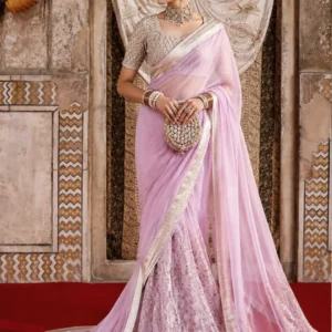 Pastel Pink Designer Saree – Elegant Indian Couture for Weddings & Special Occasions Step into timeless elegance with this Pastel Pink Designer Saree with Embroidered Blouse, a sophisticated creation designed for women who appreciate graceful silhouettes, delicate detailing, and refined Indian couture. Featuring a soft pastel pink colour palette, an intricately embellished blouse, an elegant saree drape, and a beautifully detailed lower section, this ensemble brings together traditional Indian craftsmanship and contemporary luxury styling. The delicate pastel pink shade creates a soft, feminine appearance while allowing the intricate detailing of the outfit to become the centre of attention. The saree is finished with an elegant metallic-toned border that beautifully defines the drape and adds a subtle luxurious touch. The coordinated blouse features detailed embroidery and embellishment, creating a polished look that works beautifully for weddings, receptions, engagement celebrations, festive gatherings, cocktail evenings, and sophisticated social occasions. Designed by Maharani Designer Boutique, this outfit reflects the beauty of Indian occasion wear where colour, craftsmanship, silhouette, and finishing come together to create a memorable ensemble. Whether you are looking for a designer saree for a wedding, a pastel saree for a reception, or an elegant Indian outfit for a special celebration, this design offers a luxurious and graceful choice. A Soft Pastel Pink That Makes a Statement Pastel pink continues to be one of the most elegant colour choices for contemporary Indian occasion wear. Unlike brighter shades that create an instantly dramatic appearance, pastel pink brings softness, sophistication, and understated glamour to your overall look. This particular shade works beautifully with the detailed embellishments of the ensemble. The light pink base creates a refined canvas against which the intricate embroidery and border detailing stand out naturally. It is a colour that can transition effortlessly from daytime celebrations to evening events depending on how you style your jewellery, makeup, hairstyle, and accessories. For women who want a pastel pink saree for a wedding, this design offers a graceful alternative to traditional reds, maroons, and deeper jewel tones. It can also be an excellent choice for engagement functions, wedding receptions, sangeet celebrations, festive dinners, anniversary celebrations, and elegant family occasions. The softness of the colour makes the ensemble especially suitable for women who prefer a sophisticated appearance without excessive visual heaviness. Intricately Embellished Designer Blouse The blouse is one of the defining features of this ensemble. Designed with detailed embellishment throughout the bodice and sleeves, it adds richness to the otherwise soft pastel colour story. The intricate patterning creates a beautifully textured appearance and gives the blouse a couture-inspired finish. The short-sleeved silhouette complements the saree drape while maintaining a classic Indian aesthetic. The neckline is designed to create a graceful frame around the face and neck, making the blouse especially suitable for statement jewellery. Pair it with a traditional choker, layered necklace, chandbali earrings, or elegant drop earrings for a more elevated wedding look. The blouse detailing also ensures that the outfit looks beautiful even when the saree pallu is styled in a different way. For occasions where you want the blouse to become more visible, the saree can be draped to highlight its embroidery and neckline. At Maharani Designer Boutique, designs can be developed with attention to the individual customer's preferred fit, styling requirements, and occasion, subject to the specific product and customisation selected. Elegant Saree Drape The saree has been styled in a fluid drape that creates an effortlessly feminine silhouette. The lightweight visual appearance of the drape allows the pastel pink colour to flow naturally around the body while the structured border gives definition to the overall ensemble. The border is an important element of the design. Its metallic-toned finish contrasts subtly with the pastel base and creates a sophisticated outline along the saree. As the border moves across the shoulder, front, and lower drape, it gives the outfit a beautifully finished appearance. The pallu falls gracefully from the shoulder and extends towards the floor, creating an elegant elongated silhouette. This makes the ensemble particularly suitable for photographs, wedding entrances, receptions, and formal celebrations where the overall presentation of the outfit matters. The saree can be styled traditionally or adapted to suit a more contemporary draping preference. Detailed Lower Panel for a Couture-Inspired Appearance One of the most striking elements of this ensemble is the richly detailed lower portion visible beneath the saree drape. The coordinated pastel-toned panel features intricate floral-inspired embellishment that adds depth, texture, and visual interest to the outfit. This detailing creates a beautiful contrast between the softer flowing saree and the more structured embroidered section underneath. The result is a layered appearance that resembles the sophistication of modern couture while retaining the timeless identity of a traditional Indian saree. The lower detailing also creates movement when walking, making the outfit particularly attractive for special occasions and photography. The overall composition is carefully balanced. The pastel pink colour keeps the design elegant and feminine, while the embroidery, embellishment, and border provide enough richness for a luxury occasion. Perfect for Weddings and Receptions This designer pink saree can be styled for several wedding-related occasions. Its soft colour and intricate detailing make it versatile enough to work for both daytime and evening celebrations. Wear it for a wedding reception with statement jewellery and a sleek hairstyle for a sophisticated appearance. For an engagement ceremony, pair it with delicate jewellery and soft makeup to highlight the pastel tones. For a sangeet or festive evening, you can add more dramatic earrings, a statement clutch, and glamorous makeup. The same outfit can also work beautifully for an intimate wedding celebration where you want to look elegant without choosing a heavily traditional bridal colour. This design can also be considered for: Wedding receptions Engagement ceremonies Sangeet celebrations Mehendi functions Cocktail evenings Festive celebrations Family weddings Anniversary celebrations Luxury dinner events Fashion events Traditional celebrations Destination wedding functions Pre-wedding celebrations Formal Indian occasions Jewellery Styling The right jewellery can transform the overall personality of this saree. For a traditional wedding appearance, style the pastel pink saree with a statement choker and matching earrings. The embellished blouse provides the perfect foundation for jewellery that sits around the neckline. If you prefer a more contemporary look, choose long drop earrings and skip the necklace. This allows the blouse detailing and neckline to remain visible while creating a clean and sophisticated appearance. Pearl-inspired jewellery can complement the softness of pastel pink beautifully. Traditional gold-toned jewellery can create a richer Indian aesthetic, while diamond-inspired or crystal jewellery can make the outfit feel more modern and glamorous. Bangles can be stacked for a traditional wedding appearance, while a smaller selection of bracelets can create a more contemporary styling. Hairstyle Suggestions A sleek bun is an elegant choice for this saree, especially when paired with statement earrings and a traditional jewellery set. A low bun decorated with flowers can create a graceful Indian wedding appearance. For a more modern look, wear your hair in soft waves or a polished low ponytail. These styles allow the saree and blouse detailing to remain the focus. A centre-parted hairstyle with a neat bun can give the outfit a classic traditional character, while a side-parted hairstyle can make the overall appearance feel softer and more contemporary. Makeup Styling Pastel pink outfits pair beautifully with fresh, luminous makeup. A soft neutral or pink-toned eyeshadow can complement the colour palette without overpowering the outfit. Defined eyes, natural-looking skin, softly sculpted cheeks, and a rosy or nude-pink lip can create an elegant daytime appearance. For an evening reception, you can intensify the eye makeup slightly and add a more luminous finish. A soft pink, mauve, nude, or rose-toned lipstick can work beautifully with the pastel colour story. The goal is to keep the makeup balanced so that the intricate blouse and saree detailing remain the visual focus. Why Choose a Designer Saree? A designer saree is more than simply a traditional garment. It is a carefully developed combination of colour, silhouette, embroidery, embellishment, draping, and finishing. This pastel pink ensemble demonstrates how traditional Indian dressing can be interpreted through a modern luxury lens. Instead of relying solely on heavy colours or excessive embellishment, the design uses a soft colour palette and detailed craftsmanship to create an elegant statement. For women searching for a designer saree online, the most important consideration is often the balance between appearance and versatility. An outfit that looks beautiful in photographs but is difficult to style may have limited practical value. This design offers several styling possibilities, allowing you to personalise the final appearance through jewellery, makeup, hairstyle, and draping. Ideal for the Modern Indian Woman Today's Indian woman often wants traditional clothing that feels sophisticated, comfortable, and contemporary at the same time. This pastel pink saree captures that balance. It retains the classic elegance of a saree while incorporating a refined colour palette and couture-inspired detailing. It can be styled for a traditional family wedding or a modern reception. It can be paired with classic jewellery or contemporary accessories. It can be presented with a traditional hairstyle or a modern beauty look. This versatility makes it a valuable addition to an occasion-wear wardrobe. A Beautiful Choice for Reception Wear Reception outfits often require a slightly more glamorous approach than daytime wedding clothing. This pastel pink designer saree is particularly suited to reception styling because the colour remains sophisticated while the embroidery and embellishment provide the required richness. For a glamorous reception appearance, style the saree with statement earrings, a sleek hairstyle, luminous makeup, and an embellished clutch. For a more understated reception look, choose minimal jewellery and let the blouse embroidery and saree border provide the visual interest. The result can be elegant, sophisticated, and effortlessly photogenic. Custom-Made Styling at Maharani Designer Boutique Maharani Designer Boutique specialises in creating elegant Indian occasion wear with an emphasis on craftsmanship, detailed finishing, and personalised styling. For customers who prefer a made-to-measure experience, selected designs can be customised according to measurements, preferred fitting, styling requirements, and occasion, depending on the product. Customisation can be discussed for elements such as blouse fitting, sleeve preferences, neckline preferences, styling, and other design requirements where applicable. If you are purchasing an outfit for a specific wedding date, it is recommended to discuss your event date and requirements with the boutique in advance so that the appropriate production timeline can be confirmed. Designer Saree for Indian Weddings Indian weddings are celebrations where clothing becomes an important part of the occasion. From the bride and bridesmaids to family members and wedding guests, every celebration creates an opportunity to express personal style. A pastel pink saree offers a sophisticated option for women who want something elegant and luxurious without choosing a conventional bridal-red palette. The colour is especially attractive for wedding guests, mothers of the bride or groom, sisters, cousins, bridesmaids, and women attending formal wedding receptions. Its timeless colour story also makes it less dependent on seasonal trends, allowing it to remain relevant beyond a single wedding season. Perfect for Festive Dressing Although this outfit is ideal for weddings, it is not limited to bridal occasions. The elegant colour and detailed craftsmanship make it suitable for festive celebrations such as Diwali gatherings, family celebrations, cultural events, formal dinners, and special occasions. Depending on the accessories, the same saree can look traditional, contemporary, glamorous, or understated. This adaptability makes it a beautiful choice for women who prefer investing in carefully designed occasion wear rather than selecting outfits for only one specific event. Styling for Destination Weddings Pastel shades are particularly beautiful for destination wedding photography. Whether the celebration takes place in a heritage venue, luxury hotel, palace-inspired setting, or outdoor wedding location, pastel pink creates a soft and sophisticated visual effect. The saree's flowing drape and detailed lower panel can add movement to photographs, while the embellished blouse creates a polished appearance in close-up portraits. For destination wedding styling, pair the ensemble with lightweight statement jewellery, a structured clutch, and a sleek hairstyle. A Timeless Addition to Your Wardrobe Fashion trends change, but certain silhouettes and colours remain timeless. The saree is one of India's most enduring garments, and pastel shades have become increasingly popular among modern women looking for elegant occasion wear. This ensemble combines both elements. Its traditional saree silhouette ensures timeless appeal, while the pastel pink palette and refined embellishment provide a contemporary finish. Whether worn this wedding season or styled years later for another celebration, the design can remain a sophisticated part of your occasion wardrobe. Quality and Craftsmanship At Maharani Designer Boutique, the beauty of an outfit lies not only in its visual appearance but also in the craftsmanship behind the finished garment. Intricate embroidery and embellishment require careful attention to placement, balance, and finishing. The overall design is created to ensure that the detailing complements the silhouette rather than overwhelming it. The result is an ensemble that feels luxurious while maintaining an elegant visual balance. Please note that the exact fabric composition, embroidery technique, embellishment materials, and customisation options may vary according to the final product version. Customers are encouraged to confirm product specifications, availability, measurements, and customisation requirements with the boutique before placing an order. Shop Designer Sarees Online If you are searching for designer sarees online, Indian designer sarees, wedding sarees, or pastel pink sarees for special occasions, this ensemble offers a sophisticated option for your wardrobe. Maharani Designer Boutique provides personalised assistance for customers looking for premium Indian occasion wear. Whether you are shopping from Jalandhar, another city in India, or overseas, you can discuss your preferred design, measurements, event requirements, and delivery needs with the boutique. The boutique also caters to customers looking for Indian ethnic wear for weddings and celebrations across different locations. Suitable for Global Indian Celebrations Indian fashion has become an important part of celebrations around the world. Weddings, receptions, Diwali parties, cultural gatherings, engagement functions, and family events are celebrated by Indian communities across Canada, the USA, the UK, Australia, New Zealand, and other countries. A sophisticated saree like this can be an excellent choice for customers living outside India who want authentic Indian occasion wear with a contemporary aesthetic. The soft pastel palette also works particularly well for international wedding settings, where Indian traditional clothing can be styled alongside modern luxury fashion. Final Styling Inspiration Imagine this pastel pink designer saree paired with a statement choker, delicate earrings, stacked bangles, a sleek low bun, glowing makeup, and an embellished clutch. For a daytime event, keep the styling soft and elegant. For an evening reception, increase the jewellery and add a more glamorous makeup look. For a destination wedding, choose lightweight accessories and let the flowing saree drape create movement. For an intimate family celebration, keep the jewellery minimal and allow the detailed blouse and border to speak for themselves. The possibilities are endless because the design itself provides a sophisticated foundation for personal styling. Order Your Pastel Pink Designer Saree Make your next celebration memorable with a beautifully detailed Pastel Pink Designer Saree with Embroidered Blouse, created for women who appreciate elegance, craftsmanship, and sophisticated Indian fashion. From the soft pastel colour to the intricate blouse detailing, flowing saree drape, elegant border, and richly embellished lower section, every element contributes to a refined occasion-wear aesthetic. Whether you are attending a wedding reception, engagement, sangeet, festive celebration, or another special event, this designer saree offers a graceful and luxurious way to make an impression. Explore the latest collection from Maharani Designer Boutique and discover thoughtfully designed Indian ethnic wear created for memorable occasions. For product availability, measurements, customisation, pricing, production timeline, and shipping details, contact the boutique directly before placing your order. Maharani Designer Boutique Jalandhar, Punjab, India Worldwide & PAN India shipping available WhatsApp: +91 7626902441 | +91 8699101094 Product Highlights Pastel pink designer saree ensemble Intricately embellished blouse Elegant metallic-toned saree border Detailed lower embroidered panel Sophisticated feminine colour palette Ideal for weddings and receptions Suitable for engagement and sangeet functions Perfect for festive and formal occasions Contemporary interpretation of traditional Indian saree styling Customisation may be available depending on requirements Suitable for Indian and international customers Designed by Maharani Designer Boutique Pastel pink saree, pastel pink designer saree, designer saree, designer sarees online, wedding saree, wedding sarees online, reception saree, designer wedding saree, Indian designer saree, luxury saree, party wear saree, embroidered saree, embroidered blouse saree, pink saree for wedding, pastel saree for wedding, designer saree for reception, Indian ethnic wear, luxury Indian clothing, designer boutique sarees, saree boutique in Jalandhar, designer boutique Jalandhar, Indian designer wear, wedding guest saree, engagement saree, sangeet saree, festive saree, premium saree, custom made saree, designer saree India, Maharani Designer Boutique.