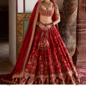 Rangrez Riwaayat – A Regal Red Bridal Lehenga by Maharani Designer Boutique Make your most treasured celebrations unforgettable with Rangrez Riwaayat, a magnificent red bridal lehenga choli created for the modern bride who loves the richness of traditional Indian fashion. Designed by Maharani Designer Boutique, this statement ensemble combines a vibrant red lehenga, intricately embellished blouse, ornate borders and a matching red dupatta to create a timeless bridal silhouette. The design celebrates the classic beauty of red and gold, one of the most enduring combinations in South Asian bridal fashion. Rich red creates an instantly festive and regal appearance, while the intricate gold-toned embroidery adds depth, dimension and luxurious detailing throughout the ensemble. From the embroidered blouse and flowing skirt to the beautifully finished dupatta, every visible element contributes to a coordinated bridal look. The lehenga is designed with a generous flare, allowing the embroidery to move beautifully with the bride and creating an elegant silhouette for wedding photographs, bridal entrances and celebrations. Rangrez Riwaayat is an ideal choice for brides searching for a red bridal lehenga, designer wedding lehenga, traditional bridal lehenga choli or an elaborate Indian wedding outfit that combines heritage-inspired styling with a sophisticated designer finish. The Timeless Appeal of Red Bridal Wear Red has an unmistakable presence in Indian bridal fashion. It has long been associated with celebration, romance, prosperity and the grandeur of wedding ceremonies. Rangrez Riwaayat embraces this traditional aesthetic with a rich red colour story that immediately establishes a luxurious bridal mood. The deep red base provides the perfect canvas for the elaborate golden embroidery. The contrast between the two colours gives the outfit a powerful visual identity while keeping the overall design rooted in traditional bridal aesthetics. Whether worn during the wedding ceremony, bridal portraits or a grand reception, the colour creates an elegant presence. The red palette is also exceptionally versatile when paired with traditional jewellery. Gold, kundan, polki, pearls and green-accented bridal jewellery can all complement the ensemble beautifully. Intricately Embroidered Bridal Lehenga The lehenga is the centrepiece of Rangrez Riwaayat. Its wide, flowing silhouette creates the classic bridal shape associated with grand Indian wedding fashion. The skirt features elaborate gold-toned embroidery arranged across the panels, creating a beautiful sense of rhythm and movement. Floral and ornamental motifs are distributed throughout the skirt, while the lower section receives additional decorative detailing. This layered approach to embroidery ensures that the lehenga looks detailed from both a distance and close up. The generous flare is particularly effective during movement. As the bride walks, turns or poses for photographs, the embroidered panels open and create a dramatic, flowing silhouette. The skirt is completed with an ornate lower border that provides a strong visual finish. Elaborate Gold-Toned Embroidery The golden embroidery gives Rangrez Riwaayat its regal character. The detailing appears across the blouse, skirt and dupatta, creating continuity between all three components. The lehenga features traditional ornamental patterns and floral-inspired motifs, giving the skirt a richly decorated appearance without relying on a single repetitive design. The embroidery also provides texture against the red foundation. Under warm wedding lighting, these decorative details can create subtle highlights as the bride moves, making the outfit especially attractive for evening celebrations and photography. The intricate embroidery gives the ensemble the visual richness expected from a statement bridal outfit. Statement Lehenga Border The lower border of the lehenga adds another layer of traditional detailing. The border creates a defined finish around the skirt and helps visually frame the overall silhouette. Its elaborate decorative pattern complements the embroidery above it and gives the lehenga a polished, luxurious appearance. The border is especially important in seated bridal portraits because it remains visible around the lower portion of the outfit. When the bride walks, the border moves with the flare, creating an elegant finishing detail. Designer Bridal Blouse The matching blouse is designed to balance the dramatic volume of the lehenga. It features a rich red base with dense gold-toned embroidery across the bodice. The neckline has been framed with decorative detailing, creating a natural focal point around the face and providing an elegant foundation for a bridal necklace. The short sleeves are also embellished, allowing the embroidery to continue around the arms. The blouse works beautifully with traditional bridal jewellery, particularly statement necklaces and layered chokers. Its fitted appearance creates a balanced contrast with the flowing lehenga, resulting in a classic bridal silhouette. Embellished Sleeves The blouse sleeves feature coordinated embroidery, adding refinement to the upper portion of the outfit. The decorative work around the sleeves becomes particularly attractive when paired with bridal bangles and bracelets. For a traditional bridal look, style the sleeves with stacked bangles in red, gold and complementary shades. For a more contemporary appearance, choose fewer but larger statement bangles or a single cuff-style bracelet. The Matching Red Dupatta The dupatta completes the Rangrez Riwaayat ensemble. It features a red base that coordinates seamlessly with the lehenga and blouse, along with an ornate embroidered border. Delicate motifs are distributed across the body of the dupatta, while the border provides a more concentrated decorative finish. The result is a dupatta that can be styled traditionally over the head or more freely across the shoulder. For the wedding ceremony, draping the dupatta over the head creates a classic bridal appearance. For the reception, it can be styled over one shoulder to showcase more of the blouse and lehenga. Bridal Dupatta Draping Ideas Traditional Head Drape Place the dupatta over the head and allow the embroidered border to frame the face. This creates an elegant and traditional bridal appearance. One-Shoulder Drape Drape the dupatta over one shoulder and let it fall naturally toward the floor. This styling allows the lehenga embroidery to remain prominent. Double Dupatta Styling If desired and suitable for the outfit, a second lightweight dupatta can be introduced for a more elaborate bridal look, subject to styling preferences and product configuration. Front Draping Allow the dupatta to fall toward the front to highlight its ornate border. A Classic Red-and-Gold Bridal Combination The red-and-gold combination gives this lehenga a distinctly traditional personality. Gold jewellery naturally complements the embroidery, while red bridal accessories can reinforce the colour story. For a classic Indian bridal appearance, consider pairing Rangrez Riwaayat with: Gold kundan jewellery Polki necklace Traditional maang tikka Bridal nath Gold jhumkas Red and gold bangles Traditional chooda Embellished potli Gold or red footwear For additional contrast, green jewellery accents can be introduced through emerald-inspired stones or green bangles. Ideal Bridal Jewellery A heavily embroidered red lehenga provides the perfect foundation for statement jewellery. Kundan Necklace A broad kundan necklace or choker can beautifully frame the neckline. Polki Jewellery Polki pieces can add an old-world royal character to the bridal appearance. Maang Tikka A traditional maang tikka enhances the centre-parted bridal hairstyle. Jhumkas Large gold jhumkas complement the ornate embroidery. Bridal Nath A traditional nath can add an unmistakable bridal touch. Bangles Stacked red and gold bangles or a traditional bridal chooda complete the look. Hairstyle Inspiration Rangrez Riwaayat works beautifully with traditional hairstyles. Classic Bridal Bun A sleek low bun provides an elegant foundation for the dupatta and bridal jewellery. Floral Bun Add traditional flowers around the bun for a timeless wedding appearance. Centre-Parted Hairstyle A centre part works particularly well with a maang tikka or matha patti. Soft Waves For a reception or engagement, soft waves can provide a more contemporary styling direction. Braided Bridal Hairstyle A long braid decorated with traditional accessories can create a distinctly Indian bridal aesthetic. Bridal Makeup Suggestions The rich red colour allows both traditional and contemporary makeup styles. For a classic bridal look, consider warm-toned eyeshadow, defined eyeliner, full lashes, glowing skin and a red or deep rose lip. For a modern bridal appearance, use softer neutral eyeshadow with luminous skin and a muted rose lip. The makeup can be adapted according to the wedding venue, lighting and personal style. Because the outfit itself features substantial embroidery, balanced makeup can help maintain an elegant overall appearance. Perfect for the Wedding Ceremony Rangrez Riwaayat is naturally suited to the main wedding celebration. The traditional red colour creates an unmistakably bridal identity, while the gold embroidery adds grandeur. The flowing lehenga also creates a beautiful silhouette for bridal entry photographs. For the ceremony, style the dupatta over the head and pair it with a traditional jewellery set, maang tikka, nath and bangles. The result is a timeless bridal look that celebrates traditional Indian wedding aesthetics. Reception Styling The same outfit can be styled differently for the reception. Instead of covering the head, drape the dupatta over one shoulder. Pair the ensemble with a statement necklace, chandelier earrings and a polished hairstyle. A more contemporary makeup look can further transform the outfit. This styling keeps the elaborate embroidery visible while giving the bride a glamorous reception appearance. Engagement & Pre-Wedding Celebrations Although designed with bridal grandeur in mind, Rangrez Riwaayat can also work beautifully for a grand engagement or pre-wedding celebration. For these occasions, consider styling it with lighter jewellery. A statement choker, earrings and bangles can create a polished appearance without making the look feel overly ceremonial. For a sangeet, the flowing lehenga silhouette also provides a dramatic presence during photographs and celebrations. Bridal Photoshoot Potential The elaborate embroidery and dramatic flare make this ensemble particularly suitable for bridal photography. For full-length photographs, allow the lehenga to spread naturally. For close-up portraits, highlight the embroidered blouse, neckline and jewellery. For traditional photographs, place the dupatta over the head. For editorial-style photographs, drape the dupatta over one shoulder and allow its embroidered border to fall naturally. The rich red colour also pairs beautifully with palace-inspired interiors, traditional architecture, floral décor and warm lighting. Bridal Entry Look The generous lehenga flare makes Rangrez Riwaayat an excellent option for a dramatic bridal entry. As the bride walks, the skirt moves naturally and allows the embroidered panels to become visible. The dupatta can be allowed to flow behind the bride or carried carefully at one side. For photography, a gentle walking pose can capture the movement of the embroidery and border. Styling with Traditional Accessories Traditional accessories can enhance the heritage character of this outfit. Consider adding: Kaleere Chooda Bridal nath Maang tikka Matha patti Kundan jewellery Embroidered potli Traditional juttis Gold waist belt, if desired Bridal hair accessories These details can be selected according to the bride's individual styling preferences. Footwear Recommendations Complete the outfit with footwear that complements the red and gold palette. Recommended options include: Gold heels: Ideal for a sophisticated reception look. Embellished sandals: Suitable for glamorous evening events. Punjabi juttis: Perfect for traditional styling. Gold mojaris: A classic ethnic choice. Red embellished footwear: Creates a coordinated bridal appearance. Comfort should remain a priority, particularly for the wedding ceremony and extended celebrations. A Versatile Designer Bridal Ensemble One of the key strengths of Rangrez Riwaayat is its styling versatility. The same outfit can look traditional, regal, glamorous or contemporary depending on the accessories. For a traditional ceremony, use a head-draped dupatta and elaborate jewellery. For the reception, style the dupatta over one shoulder with statement earrings. For a photoshoot, create an editorial silhouette with minimal accessories. For an engagement, use lighter jewellery and a softer hairstyle. This versatility makes the outfit suitable for multiple important wedding moments. Designed for the Modern Maharani Rangrez Riwaayat takes inspiration from the grandeur associated with the word Maharani—royal elegance, detailed ornamentation and timeless Indian fashion. At the same time, its styling possibilities allow the contemporary bride to personalize the ensemble. The outfit can be styled according to individual preferences while retaining its traditional identity. It is designed for the woman who wants to celebrate heritage while expressing her own fashion personality. Why Choose Maharani Designer Boutique? Maharani Designer Boutique creates occasion-wear inspired by the beauty of Indian ethnic fashion. The brand focuses on designs that combine rich colour palettes, intricate embellishment, traditional silhouettes and contemporary styling possibilities. Rangrez Riwaayat represents this aesthetic through its red bridal colour, elaborate gold embroidery, flowing lehenga, embellished blouse and coordinated dupatta. The result is a statement ensemble designed for women who want their special occasion wardrobe to feel memorable and luxurious. Customisation & Fitting A bridal outfit should provide an elegant silhouette while allowing comfortable movement. If customisation is available for this design, measurements may be required for the blouse and other components. Potential measurements may include: Bust Waist Shoulder Sleeve length Blouse length Lehenga waist Lehenga length Desired fit Customisation availability may depend on the design and production requirements. For wedding orders, customers should confirm measurements and required delivery timelines with Maharani Designer Boutique before placing the order. Care Instructions Intricately embellished bridal wear should be handled carefully. Store the outfit in a clean and breathable garment bag. Avoid placing heavy garments over the embroidered areas. Keep the outfit away from moisture, perfumes and excessive humidity. Do not wash or iron heavily embellished sections without checking the appropriate care method. Professional garment care may be recommended depending on the final fabric and embellishment. When storing the dupatta, fold it carefully to protect its decorative border. For transportation, use suitable garment protection to minimize friction and snagging. Product Details Product Name: Rangrez Riwaayat Brand: Maharani Designer Boutique Product Category: Bridal Lehenga Choli Primary Colour: Rich Red Embroidery: Gold-Toned Traditional Embroidery Blouse: Embroidered Red Bridal Blouse Lehenga: Flared Red Embroidered Lehenga Dupatta: Matching Red Dupatta with Embellished Border Style: Traditional, Regal, Luxurious & Bridal Occasions: Wedding, Reception, Engagement, Sangeet, Bridal Entry, Photoshoot & Festive Celebrations Overall Aesthetic: Classic Indian Bridal Luxury red bridal lehenga, red bridal lehenga choli, red wedding lehenga, red bridal dress, red lehenga for bride, red lehenga for wedding, red and gold bridal lehenga, red gold lehenga, gold embroidered bridal lehenga, heavily embroidered bridal lehenga, designer bridal lehenga, designer wedding lehenga, traditional bridal lehenga, traditional red bridal lehenga, Indian bridal lehenga, Indian wedding lehenga, bridal lehenga online, bridal lehenga India, wedding lehenga for bride, bridal wear for women, designer bridal wear, red bridal outfit, red wedding outfit, bridal lehenga with dupatta, red lehenga with dupatta, bridal lehenga choli, embroidered lehenga choli, luxury bridal lehenga, luxury Indian bridal wear, bridal wedding outfit, bridal reception lehenga, reception lehenga for bride