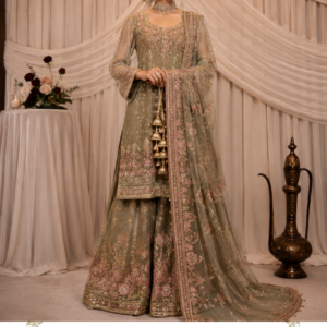 Sage Green Embroidered Sharara Suit – Noor-e-Gul Sage by Maharani Designer Boutique Discover the graceful beauty of Noor-e-Gul Sage, an elegant sage green embroidered sharara suit created for women who appreciate sophisticated Indian ethnic fashion with a luxurious contemporary finish. Designed by Maharani Designer Boutique, this ensemble brings together a soft sage green palette, delicate pink floral embroidery, intricate borders and a beautifully coordinated sheer dupatta to create a refined occasion-wear look. The outfit captures a romantic and sophisticated aesthetic through its muted green base and delicate blush-pink embellishment. Unlike heavily saturated festive colours, the sage green tone offers an understated elegance that works beautifully for daytime celebrations, intimate weddings, festive gatherings, engagement ceremonies and sophisticated evening occasions. The silhouette combines a beautifully embroidered kurta with a flowing sharara and matching dupatta. Each component contributes to the overall richness of the outfit while maintaining a graceful balance between embroidery, colour and fabric movement. The kurta features a softly structured silhouette with an elegant neckline and long sleeves. Delicate floral embroidery is concentrated around the neckline and continues across the front, sleeves and lower hem. The sharara carries coordinating floral embroidery toward the lower portion, while the sheer dupatta features scattered floral motifs and an ornate embroidered border. Together, these elements create an ensemble that feels feminine, luxurious and effortlessly elegant. A Sophisticated Sage Green Colour Palette The defining feature of Noor-e-Gul Sage is its beautiful sage green colour. Sage green is a versatile shade that sits between muted green and soft neutral tones. Its subtle character makes it especially suitable for women who want an elegant alternative to traditional bright festive colours. The sage base allows the intricate embroidery to remain the visual focus while creating a calm and sophisticated overall appearance. The addition of soft pink floral details introduces a romantic contrast. The combination of sage green, blush pink and metallic embroidery creates a graceful colour story that can transition easily between daytime and evening events. This colour palette is particularly suitable for: Engagement ceremonies Mehendi functions Day weddings Wedding guest dressing Family celebrations Festive gatherings Anniversary celebrations Elegant dinner events Formal ethnic occasions Pre-wedding celebrations Intimate wedding functions Traditional photoshoots The muted palette also gives you plenty of flexibility when selecting jewellery, footwear, makeup and accessories. Intricate Floral Embroidery Floral embroidery is at the heart of the Noor-e-Gul Sage design. The front of the kurta features elaborate floral motifs arranged across the bodice and lower section. The embroidery combines fine botanical-inspired patterns with delicate pink accents and metallic detailing. The floral arrangement creates visual continuity across the outfit rather than appearing as isolated decorative elements. The neckline receives special attention, with embroidery framing the upper portion of the kurta and naturally drawing attention toward the face. Additional detailing extends along the sleeves, cuffs and hem, creating a coordinated appearance. The embroidery is particularly beautiful when viewed up close because the combination of fine floral forms and subtle colour variation creates depth across the sage green base. Elegant Sharara Silhouette The sharara adds movement and volume to the outfit. Unlike a straight trouser silhouette, the flowing sharara creates a graceful, feminine shape that moves beautifully while walking. The lower portion is decorated with coordinated floral embroidery and a detailed border. This gives the sharara a statement finish without overwhelming the overall outfit. The wider silhouette also complements the fitted or softly structured upper portion of the kurta, creating a balanced ethnic silhouette. The sharara can be paired with traditional juttis for a classic look or elegant heels for a more contemporary styling approach. Beautifully Detailed Kurta The kurta forms the central component of this three-piece ensemble. Its design features a graceful neckline, long sleeves and an embroidered front. The embroidery is distributed carefully across the kurta so that the design remains detailed without appearing excessively heavy. The front features delicate floral compositions, while the lower hem is finished with an ornate embroidered border. This combination gives the kurta an elegant, finished appearance. The sleeves are also embellished, adding sophistication to the overall silhouette. The sleeve cuffs feature concentrated embroidery that creates a decorative finish around the wrists. This makes the outfit especially attractive when paired with bangles or statement bracelets. Statement Embroidered Dupatta The sheer dupatta adds an important layer of elegance to Noor-e-Gul Sage. Its lightweight appearance creates a soft contrast against the more structured kurta and sharara. The dupatta features delicate scattered floral motifs throughout its body, allowing the sage green colour to remain visible while adding subtle decorative detail. The border is more heavily embroidered, creating a beautiful frame around the flowing fabric. When worn over one shoulder, the embroidered border creates a graceful vertical line that complements the silhouette. When draped over both shoulders, it creates a more traditional ethnic appearance. For wedding functions, the dupatta can also be styled over the head for a modest and graceful look. Floral Pink Embellishment The soft pink embroidery is one of the most charming elements of this design. Rather than using a strong contrasting colour, the embroidery incorporates a delicate blush-like tone that blends naturally with the sage base. This creates a romantic and feminine appearance. The pink floral detailing can be complemented with jewellery featuring: Rose-toned stones Pearls Polki Kundan Gold accents Champagne-toned embellishments Soft pink stones The result is an outfit that feels elegant without appearing overly dramatic. Perfect for Wedding Guests Noor-e-Gul Sage is an excellent choice for wedding guests who want to look dressed-up and sophisticated without choosing a traditional bridal colour palette. The combination of sage green and pink gives the outfit a fresh and contemporary appearance. For a wedding guest look, style it with delicate earrings, a sleek hairstyle and embellished footwear. A small clutch or potli bag can complete the ensemble. For daytime functions, keep the jewellery light and let the embroidery speak for itself. For evening celebrations, add statement earrings and a more defined makeup look. Ideal for Engagement Ceremonies Engagement celebrations often call for outfits that are festive but slightly more understated than bridal wear. The Noor-e-Gul Sage sharara suit fits this aesthetic beautifully. The floral embroidery gives the ensemble a celebratory character, while the muted sage colour maintains sophistication. Pair it with a statement choker, chandelier earrings and soft waves for an elegant engagement look. Alternatively, a traditional bun decorated with flowers can give the ensemble a more classic Indian appearance. Beautiful Mehendi & Festive Look The fresh green tone makes this outfit particularly suitable for mehendi celebrations. Sage green has a natural association with botanical and floral aesthetics, making it an elegant choice for garden-inspired or daytime functions. For mehendi styling, pair the outfit with: Floral jewellery Pearl accessories Green bangles Soft pink earrings Embellished juttis Floral hair accessories A loose braid or soft waves can enhance the relaxed festive character of the outfit. Day Wedding Styling For a daytime wedding, the muted colour palette can look especially beautiful in natural light. The delicate embroidery catches the light subtly without creating an overly heavy appearance. Pair Noor-e-Gul Sage with pearl or kundan jewellery for a refined wedding guest look. For footwear, choose champagne, gold or pastel-toned embellished sandals. Keep makeup luminous and fresh with soft eyes, natural blush and a muted rose lip. Evening Styling The same outfit can easily be transformed into an evening ensemble. Choose more dramatic jewellery and a polished hairstyle. A statement choker or long necklace can add additional glamour. Pair it with chandelier earrings and metallic heels. For makeup, defined eyes, luminous skin and a rose or mauve lip can complement the outfit beautifully. The embroidered details become particularly striking under warm evening lighting. Jewellery Pairing Because Noor-e-Gul Sage features detailed embroidery, jewellery should complement rather than compete with the outfit. Kundan Jewellery Kundan works beautifully with the traditional character of the ensemble. Pearl Jewellery Pearls provide a soft and elegant contrast against the sage green base. Gold Jewellery Gold adds warmth and enhances the metallic embroidery. Polki Jewellery For a more luxurious wedding look, pair the outfit with a traditional polki set. Floral Jewellery For mehendi or daytime functions, floral jewellery can create a fresh and youthful appearance. Hairstyle Suggestions The versatility of the outfit allows several hairstyles. Soft Waves Loose waves create a modern, romantic appearance. Low Bun A sleek low bun is ideal for formal wedding functions. Floral Bun Add fresh or artificial flowers for a traditional Indian look. Braided Hairstyle A soft braid can work beautifully for mehendi celebrations. Half-Up Hairstyle A half-up style offers a balance between traditional and contemporary styling. Makeup Inspiration The sage and pink colour combination pairs beautifully with soft, luminous makeup. For daytime occasions, consider: Fresh glowing base Soft brown eyeshadow Defined lashes Peachy-pink blush Soft rose lipstick For evening events, enhance the look with: Defined eyeliner Smoky neutral eyes Highlighter Rosy blush Mauve or rose-toned lipstick Avoid overly strong makeup if you want the embroidery and colour palette to remain the main focus. Footwear Styling The outfit can be styled with both traditional and contemporary footwear. For a classic Indian look, choose embroidered Punjabi juttis or traditional mojaris. For weddings and formal evening functions, embellished heels or metallic sandals can elongate the silhouette. Recommended shades include: Gold Champagne Nude Soft pink Beige Metallic tones A coordinated potli bag can complete the look. Occasion-Wear Versatility One of the strongest qualities of Noor-e-Gul Sage is its versatility. It can be styled differently depending on the event. For a daytime function, use minimal jewellery and natural makeup. For an engagement, add statement earrings and a choker. For a wedding, pair it with traditional jewellery and an elegant hairstyle. For a festive dinner, keep the dupatta draped over one shoulder and accessorise with metallic heels and a clutch. This makes the outfit suitable for multiple celebrations rather than being limited to one occasion. A Feminine Contemporary Indian Silhouette Noor-e-Gul Sage brings together traditional Indian clothing elements with a contemporary colour palette. The sharara silhouette remains deeply rooted in South Asian festive fashion, while the sage green and blush-pink combination gives it a modern personality. The result is a look that feels familiar yet fresh. It is ideal for women who appreciate traditional craftsmanship but prefer softer colours and elegant styling. Beautiful Dupatta Draping Options One-Shoulder Drape Place the dupatta over one shoulder and let it fall naturally along the side. This allows the embroidered kurta to remain clearly visible. Two-Shoulder Drape Drape the dupatta across both shoulders for a balanced and traditional appearance. Head Drape For a more traditional function, place the dupatta over the head and allow the embellished border to frame the face. Front Draping Bring the dupatta toward the front and allow the embroidered border to remain visible. Styling for Family Celebrations Noor-e-Gul Sage is also an excellent choice for family celebrations. Whether attending a festive dinner, anniversary, traditional ceremony or special gathering, the outfit offers a polished ethnic appearance without feeling excessively bridal. Pair it with small earrings and a delicate bracelet for a sophisticated daytime look. For a more festive appearance, add a statement necklace and embellished footwear. Photography-Friendly Details The outfit is particularly suitable for photographs because of its layered design. The flowing sharara creates movement. The embroidered kurta provides texture. The sheer dupatta adds softness. The ornate border creates strong visual definition. The sage green base photographs beautifully against neutral, floral and architectural backgrounds. For portraits, a soft natural-light setting can highlight the delicate embroidery and pink floral detailing. For evening photography, warm lighting can bring out the metallic elements of the embroidery. Maharani Designer Boutique Maharani Designer Boutique presents this ensemble for women who appreciate elegant Indian fashion, intricate detailing and sophisticated occasion wear. The design language focuses on creating outfits that combine traditional silhouettes with contemporary colour stories and refined embellishment. Noor-e-Gul Sage reflects that aesthetic through its graceful sharara silhouette, floral embroidery, detailed borders and elegant dupatta. The result is an outfit designed to help you feel polished, feminine and beautifully dressed for important celebrations. Why Choose Noor-e-Gul Sage? Choose this ensemble if you are looking for: A sophisticated sage green ethnic outfit An embroidered sharara suit A floral wedding guest outfit A stylish engagement ensemble A festive Indian outfit A contemporary traditional suit A statement embroidered dupatta A soft pastel occasion-wear look A versatile wedding outfit A graceful Maharani Designer Boutique creation Its combination of colour, embroidery and silhouette makes it a timeless addition to an occasion-wear wardrobe. Care & Storage Embroidered occasion wear should be handled carefully to preserve its decorative detailing. Store the outfit in a clean, breathable garment bag. Avoid placing heavy clothing or accessories directly over the embroidery. Keep the outfit away from moisture and excessive humidity. Do not use harsh washing methods without checking the garment's specific care requirements. Professional dry cleaning may be recommended depending on the actual fabric and embellishment. Fold the dupatta carefully and avoid placing sharp accessories against its delicate surface. When travelling, use suitable garment protection to reduce friction and creasing. Product Details Product Name: Noor-e-Gul Sage Brand: Maharani Designer Boutique Category: Designer Sharara Suit Style: Embroidered Sharara Suit Primary Colour: Sage Green Secondary Colour: Soft Pink Embroidery: Floral and Ornamental Embroidery Top: Embroidered Long-Sleeve Kurta Bottom: Coordinated Embroidered Sharara Dupatta: Sheer Embroidered Dupatta with Decorative Border Overall Style: Elegant, Feminine, Traditional & Contemporary Occasions: Wedding, Engagement, Mehendi, Festive Events, Reception, Parties & Family Celebrations Fabric composition, lining, measurements and customisation options should be confirmed according to the specific product available from Maharani Designer Boutique. sage green sharara suit, sage green sharara suit for women, green sharara suit, embroidered sharara suit, designer sharara suit, sharara suit for wedding, sharara suit for wedding guest, sharara suit for engagement, sharara suit for mehendi, floral embroidered sharara suit, sage green ethnic wear, sage green suit for women, designer ethnic wear, Indian sharara suit, Indian wedding outfit, wedding guest outfit for women, designer wedding wear, festive sharara suit, party wear sharara suit, embroidered suit for women, designer suit for women, sharara dress for women, traditional sharara suit, modern sharara suit, pastel sharara suit, pastel green sharara suit, green embroidered suit, pink and green sharara suit, Designer Sharara Suits floral suit for wedding, floral embroidered suit, designer Punjabi suit, Punjabi ethnic wear, Punjabi wedding outfit, wedding shopping outfit, Indian festive wear, women's ethnic wear, designer Indian wear, embroidered ethnic suit, luxury ethnic wear, occasion wear for women, wedding function dress, engagement dress for women, mehendi outfit for women, sangeet outfit for women, party wear Indian suit, designer boutique suit, Maharani Designer Boutique, Maharani Designer, boutique suits, designer suits, wedding suits for women, ethnic fashion India, Indian fashion boutique, designer sharara online, sharara suit online India, embroidered sharara online, sage green wedding outfit, pastel wedding outfit, elegant ethnic outfit, floral designer suit, festive designer suit.