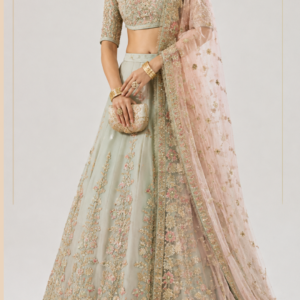 Sage Green Bridal Lehenga with Pink Dupatta Step into an enchanting world of pastel luxury with Gulbahaar Noor, an exquisitely detailed sage green and blush pink designer lehenga created by Maharani Designer Boutique. Designed for the modern bride and the sophisticated woman who appreciates delicate craftsmanship, romantic colours, intricate embroidery, and timeless Indian silhouettes, this ensemble captures the beauty of contemporary bridal fashion with a distinctly graceful character. The outfit showcases a beautifully embellished sage green lehenga paired with a heavily embroidered cropped blouse and a delicate blush pink sheer dupatta. The harmonious combination of soft sage, pastel pink, antique-gold-inspired embroidery, and delicate floral detailing creates an elegant and feminine aesthetic. The lehenga features a flowing, voluminous silhouette decorated with elaborate floral and botanical-inspired embroidery. Delicate vertical embroidered panels extend across the skirt, creating a graceful elongated effect, while the lower portion is finished with a richly embellished scalloped border. The blouse is equally detailed, featuring dense embroidery across the front and sleeves. Its cropped silhouette creates a contemporary bridal appearance while retaining the elegance of traditional Indian craftsmanship. The sheer blush pink dupatta introduces softness to the ensemble. It is decorated with delicate scattered floral motifs and framed with an elaborate embroidered border that beautifully combines the sage green, blush pink, and gold colour story. Gulbahaar Noor is designed for brides, bridesmaids, wedding guests, and women looking for sophisticated designer Indian wear for engagements, receptions, sangeet celebrations, festive occasions, and luxury wedding events. The Beauty of Pastel Sage Green Sage green is at the heart of this designer lehenga. Its muted pastel character gives the outfit a fresh, sophisticated, and contemporary personality. Unlike stronger jewel tones, sage green creates a softer visual impression while still providing enough depth for intricate embroidery to stand out. The colour works beautifully with the blush pink dupatta and pastel floral detailing. Gold-inspired embroidery adds warmth and creates a luxurious contrast against the cool sage base. This combination is especially attractive for brides who want to move beyond traditional reds and maroons while still embracing the richness of Indian bridal craftsmanship. Sage green also works beautifully for daytime celebrations. In natural light, the pastel shade creates an ethereal appearance, while warm evening lighting enhances the gold embroidery and gives the outfit a more luxurious character. Romantic Blush Pink Dupatta The blush pink dupatta provides the perfect romantic contrast to the sage green lehenga. Its sheer, lightweight appearance creates softness and movement while allowing the embroidered lehenga beneath it to remain visible. The blush pink colour complements the pastel palette beautifully. Delicate floral and ornamental motifs are scattered throughout the dupatta, giving it a graceful appearance without making it visually heavy. The border is one of the most elaborate elements of the dupatta. A wide embroidered border runs along the edges, incorporating floral motifs and traditional ornamental detailing. The border helps frame the outfit beautifully when the dupatta is draped over the shoulder. For a bridal appearance, the dupatta can be placed over the head. For a contemporary reception look, it can be draped elegantly across one shoulder. Intricate Floral Embroidery Floral embroidery defines the overall personality of Gulbahaar Noor. The lehenga features elaborate botanical-inspired patterns arranged across the skirt. Flowers, leaves, vines, and ornamental details create a garden-inspired appearance. The embroidery is arranged in vertical compositions that flow naturally from the waist towards the hem. This placement gives the skirt a graceful sense of movement and helps visually elongate the silhouette. The floral motifs are enhanced with delicate pink accents, creating subtle colour variation against the sage green base. Gold-toned detailing adds additional depth and gives the embroidery a softly luminous appearance. The result is an ensemble that feels romantic, luxurious, and timeless. Heavily Embroidered Blouse The blouse provides an elaborate focal point for the upper portion of the ensemble. Its cropped silhouette gives the outfit a contemporary bridal character while the extensive embroidery maintains its traditional identity. The entire blouse is richly decorated with floral and ornamental embroidery. The neckline is framed with detailed work that creates a refined finish around the face and collarbone. The sleeves feature matching embroidery, creating continuity between the blouse and lehenga. The blouse is designed to balance the flowing volume of the lehenga. Its structured appearance provides definition to the waist while the skirt creates movement below. Elegant Sleeves The sleeves are carefully coordinated with the blouse. They feature detailed embroidery across their length, creating a seamless connection with the heavily decorated bodice. The sleeve design adds sophistication and provides a more refined alternative to sleeveless bridal silhouettes. The three-quarter sleeve length is particularly versatile. It can work beautifully for engagement celebrations, wedding receptions, formal dinners, and traditional ceremonies. The embroidered sleeves also create attractive details in close-up photographs. Graceful Lehenga Silhouette The lehenga features a flowing, full silhouette that creates beautiful movement. Its volume allows the embroidered panels to spread naturally while walking, posing, or entering a wedding venue. The skirt is designed with multiple sections of embroidery, creating rhythm throughout the garment. The vertical floral arrangements guide the eye downwards and enhance the elegance of the silhouette. The lower section becomes increasingly elaborate, culminating in a richly embroidered border. This combination of volume and detailed embroidery creates a luxurious couture-inspired appearance. Statement Lehenga Border The hem of the lehenga is one of its most prominent design elements. A wide, intricately embroidered border runs around the bottom of the skirt. The border incorporates floral motifs, ornamental patterns, and delicate scalloped detailing. This creates a beautiful finishing effect and provides visual weight to the lower portion of the lehenga. When the skirt moves, the border becomes especially noticeable. It also photographs beautifully in full-length bridal portraits. The intricate hem gives the outfit a polished and luxurious appearance from every angle. Delicate Floral Motifs Across the Skirt The skirt features repeated floral motifs distributed between the larger embroidered panels. These smaller motifs fill the space beautifully while allowing the sage green base to remain visible. This creates a balanced composition. The embroidery does not appear randomly placed. Instead, the motifs follow an organised arrangement that creates visual continuity from the waist to the hem. The combination of larger floral elements and smaller scattered motifs gives the lehenga depth. Pastel Pink and Gold Embroidery The use of pastel pink within the embroidery adds a subtle romantic quality. Small floral elements incorporate pink tones that coordinate with the blush pink dupatta. Gold-inspired detailing provides contrast and brings warmth to the design. The three colours—sage green, blush pink, and gold—create a sophisticated pastel bridal palette. This makes the ensemble especially suitable for brides who prefer soft, elegant colours over traditional deep bridal shades. Perfect for Engagement Ceremonies Gulbahaar Noor is an excellent choice for an engagement celebration. Its pastel colour palette creates a sophisticated appearance, while the detailed embroidery provides the required festive richness. For an engagement, pair the lehenga with: Statement earrings A delicate choker Maang tikka Gold bangles Embellished clutch Soft pastel makeup A polished bun decorated with fresh flowers can complete the look. Alternatively, soft waves can create a more contemporary appearance. Dreamy Reception Look The pastel sage and blush palette is particularly beautiful for wedding receptions. For an evening reception, style the lehenga with statement jewellery featuring pearls, diamonds, kundan-inspired details, or gold tones. The sheer dupatta can be draped elegantly over one shoulder to showcase the embroidered blouse. A sleek bun and dramatic earrings can create a sophisticated bridal reception look. For a softer appearance, wear the hair in loose waves and choose delicate jewellery. Elegant Sangeet Outfit The flowing lehenga silhouette makes this ensemble suitable for sangeet celebrations. The skirt moves naturally, creating a beautiful effect while walking and dancing. For a sangeet, the outfit can be styled with statement earrings and minimal neck jewellery. The pastel colour palette gives the ensemble a youthful and sophisticated appearance. A soft pink lip, luminous skin, and subtle eye makeup can complete the look. Mehendi Celebration For a mehendi celebration, Gulbahaar Noor can be styled with floral jewellery. Choose fresh or artificial flowers in blush pink, ivory, peach, and soft green tones. This creates a romantic garden-inspired appearance that complements the floral embroidery. The lightweight dupatta can be draped over one shoulder to allow comfortable movement. A floral hair accessory can coordinate beautifully with the overall pastel colour palette. Bridal Styling For a bride who wants a softer bridal aesthetic, Gulbahaar Noor offers an elegant alternative to traditional red bridal lehengas. The sage green base creates a distinctive bridal appearance. The blush pink dupatta introduces romance. The gold embroidery provides traditional richness. The floral motifs create femininity. Together, these elements create a contemporary bridal look that remains rooted in Indian fashion. The ensemble can be particularly beautiful for intimate weddings, daytime ceremonies, garden weddings, destination weddings, and modern luxury celebrations. Wedding Guest Styling The ensemble can also be styled for wedding guests. For guests, choose lighter jewellery and a more understated makeup look. Statement earrings paired with a simple bracelet can provide enough elegance without making the outfit feel excessively bridal. A soft clutch and minimal footwear can complete the appearance. For a close family wedding, the jewellery can be made more elaborate. Jewellery Recommendations The pastel palette gives you considerable freedom when selecting jewellery. Gold jewellery works naturally with the embroidery. Kundan-inspired jewellery can create a traditional appearance. Pearls can introduce softness. Diamond-inspired accessories can give the ensemble a contemporary luxury feel. For bridal styling, consider: Statement choker Long necklace Maang tikka Jhumka earrings Bangles Statement rings Waist belt For a reception, oversized earrings and a delicate bracelet may be enough. Hairstyle Suggestions A sleek low bun is a timeless choice for this lehenga. Decorate it with fresh flowers for a traditional bridal appearance. A centre-parted bun can complement a maang tikka beautifully. For a modern reception, soft waves create a romantic appearance. A half-up hairstyle can work well for engagement and sangeet celebrations. If the dupatta is worn over the head, a neat bun provides an elegant foundation. Makeup Styling The soft pastel colours of the ensemble pair beautifully with luminous makeup. For daytime celebrations, consider: Fresh luminous skin Soft peach blush Champagne eyeshadow Brown eyeliner Natural lashes Rose-pink lipstick For evening events, add more defined eyes and a slightly deeper rose or berry lip. Gold or champagne shimmer can complement the embroidery. The makeup should enhance rather than overpower the delicate colour palette. Photography-Friendly Design Gulbahaar Noor is exceptionally suitable for bridal photography. The detailed blouse creates beautiful close-up portrait opportunities. The embroidered skirt provides texture in full-length photographs. The flowing dupatta adds movement. The pastel colour palette works beautifully with soft natural light. The outfit can be photographed against: Heritage architecture Luxury wedding venues Garden settings Neutral studio backgrounds Palace-inspired interiors Outdoor wedding décor The embroidery creates numerous details for close-up photography, while the flowing silhouette creates dramatic full-length images. Garden Wedding Aesthetic The floral embroidery and pastel colour palette make this ensemble particularly suitable for garden weddings. The sage green harmonises beautifully with natural surroundings. The blush pink dupatta introduces a romantic floral quality. The gold embroidery adds enough luxury to keep the ensemble formal. For a garden wedding, style it with floral jewellery, soft waves, and natural makeup. Destination Wedding Appeal Gulbahaar Noor is also an elegant choice for destination weddings. It can complement beachside luxury venues, heritage properties, garden resorts, palace settings, and intimate destination celebrations. The pastel colour palette photographs beautifully in natural surroundings. For daytime destination events, pair it with delicate jewellery. For evening celebrations, introduce statement gold accessories. The flowing lehenga and sheer dupatta create movement in outdoor photography. Contemporary Indian Bridal Fashion Modern bridal fashion increasingly embraces pastel colour palettes and sophisticated embroidery. Gulbahaar Noor reflects this evolution. It maintains the traditional lehenga silhouette while introducing a softer colour combination. The sage green base provides freshness. The blush pink dupatta creates romance. The gold embroidery preserves the richness of Indian bridal craftsmanship. The result is a contemporary bridal ensemble that remains timeless. Designer Indian Wear for Global Celebrations Indian weddings are celebrated across the world, and pastel designer lehengas have become a sophisticated choice for modern brides and wedding guests. Gulbahaar Noor can be styled for celebrations in India and internationally, including weddings and cultural events in Canada, the USA, the UK, Australia, New Zealand, and other destinations. The sophisticated pastel palette makes it especially suitable for multicultural weddings and luxury destination celebrations. Maharani Designer Boutique offers PAN India and worldwide shipping for customers looking for premium Indian designer wear. Custom-Made Designer Experience At Maharani Designer Boutique, selected designer ensembles may be customised or made to measure according to individual requirements. Customers can discuss measurements, blouse fitting, neckline preferences, sleeve details, lehenga length, flare, dupatta styling, and other possible customisation options depending on the design. If the outfit is being ordered for a specific wedding date, customers should share the event date before confirming the order. Production timelines can vary depending on embroidery, construction, customisation, and order requirements. A Statement Piece for the Modern Bride A bridal lehenga should represent more than a colour or trend. It should reflect the personality of the woman wearing it. Gulbahaar Noor is designed for a bride who wants elegance without relying on traditional deep-red bridal colours. It offers a softer interpretation of luxury. The embroidery remains rich and elaborate. The silhouette remains unmistakably bridal. The pastel colours give the ensemble a modern identity. This makes it ideal for brides who want their wedding wardrobe to feel personal and distinctive. Versatility Beyond the Wedding Day Although the ensemble is perfect for bridal and wedding occasions, individual components can inspire different styling options. The embroidered blouse can potentially be styled separately with a contrasting skirt or saree. The lehenga can be paired with another embellished blouse for a different occasion. The blush pink dupatta can complement other pastel ethnic outfits. This versatility makes the ensemble valuable as part of a broader designer wardrobe. Care and Storage Due to the intricate embroidery and delicate sheer dupatta, careful handling is recommended. Store the lehenga in a clean, dry garment bag. Avoid placing heavy items over embroidered sections. Fold the dupatta carefully to protect its delicate border and embellishments. For long-term bridal storage, use breathable garment packaging where possible. Professional cleaning is recommended for heavily embroidered occasion wear. The exact cleaning method should always be determined according to the final fabric and embellishment specifications. Always follow the care instructions provided with the finished outfit. Why Choose Gulbahaar Noor? Choose Gulbahaar Noor if you are searching for: A pastel green bridal lehenga Sage green designer lehenga Blush pink bridal dupatta Pastel wedding lehenga Floral embroidered lehenga Designer bridal lehenga Engagement lehenga Reception lehenga Sangeet lehenga Mehendi outfit Destination wedding lehenga Contemporary bridal wear Luxury Indian ethnic wear Custom-made designer lehenga Premium wedding fashion The Beauty of Pastel Luxury Pastel luxury is about balancing softness with craftsmanship. Gulbahaar Noor achieves this through its colour palette and detailed embroidery. The sage green creates calmness. Blush pink adds romance. Gold embroidery provides richness. Floral motifs introduce femininity. The flowing lehenga creates movement. The sheer dupatta adds softness. Together, these elements create an elegant and sophisticated bridal aesthetic. A Timeless Bridal Investment Trends change, but graceful silhouettes and beautiful craftsmanship remain relevant. The classic lehenga silhouette ensures that the ensemble retains its bridal appeal over time. The pastel colour palette gives it a contemporary character without making it overly dependent on a particular fashion trend. The floral embroidery adds timeless Indian elegance. This makes Gulbahaar Noor an ensemble that can remain meaningful long after the wedding celebration. Final Look Gulbahaar Noor is a celebration of pastel elegance, intricate craftsmanship, romantic floral embroidery, and contemporary bridal fashion. The sage green lehenga creates a sophisticated foundation, decorated with elaborate floral and botanical-inspired embroidery. The heavily embroidered blouse adds richness to the upper silhouette while maintaining a modern cropped shape. The flowing lehenga creates graceful movement, with intricate vertical motifs leading towards a statement embroidered hem. The blush pink sheer dupatta adds a soft and romantic finishing layer, decorated with delicate floral motifs and a richly embroidered border. Together, the sage green, blush pink, ivory, and gold-inspired palette creates an enchanting bridal look that is elegant, feminine, and memorable. Whether you are preparing for your engagement, sangeet, mehendi, wedding reception, destination wedding, or another grand celebration, Gulbahaar Noor offers a sophisticated interpretation of Indian bridal fashion. Discover premium designer ethnic wear from Maharani Designer Boutique, where traditional craftsmanship meets contemporary luxury. For current availability, pricing, fabric specifications, measurements, customisation, production timelines, and shipping information, contact Maharani Designer Boutique before placing your order. Product Highlights Pastel sage green designer lehenga Blush pink sheer dupatta Intricate floral embroidery Gold-toned embellished detailing Heavily embroidered blouse Three-quarter embroidered sleeves Detailed cropped blouse Flowing full-flare lehenga Vertical floral embroidery panels Elaborately embroidered lehenga hem Scalloped decorative border Delicate embroidered dupatta motifs Richly embroidered dupatta border Pastel bridal colour palette Sage green, blush pink and gold combination Contemporary bridal silhouette Ideal for engagement ceremonies Perfect for sangeet and mehendi Suitable for wedding receptions Elegant destination wedding outfit Beautiful bridal and wedding guest option Customisation may be available Made-to-measure options may be available PAN India and worldwide shipping Sage green lehenga, sage green bridal lehenga, pastel green lehenga, pastel bridal lehenga, sage green designer lehenga, sage green lehenga online, blush pink lehenga, blush pink bridal lehenga, green and pink lehenga, pastel green and pink lehenga, designer lehenga, designer bridal lehenga, floral embroidered lehenga, embroidered bridal lehenga, heavy embroidered lehenga, pastel wedding lehenga, wedding lehenga online, bridal lehenga online, engagement lehenga, reception lehenga, sangeet lehenga, mehendi lehenga, destination wedding lehenga, pastel wedding outfit, designer Indian bridal wear, luxury bridal lehenga, Indian designer lehenga, Punjabi bridal lehenga, bridal wear India, designer bridal wear Jalandhar, designer boutique Jalandhar, Maharani Designer Boutique, custom made bridal lehenga, premium Indian ethnic wear, Indian wedding outfits, bridal lehenga Canada, bridal lehenga USA, bridal lehenga UK.